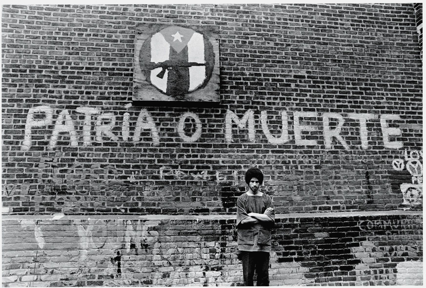 Portrait of American political and social activist Felipe Luciano and members of the Young Lords Organization (of which Luciano was a co-founder) as he stands with his arms crossed in front of a brick wall in Newark, New Jersey, July 23, 1970. 