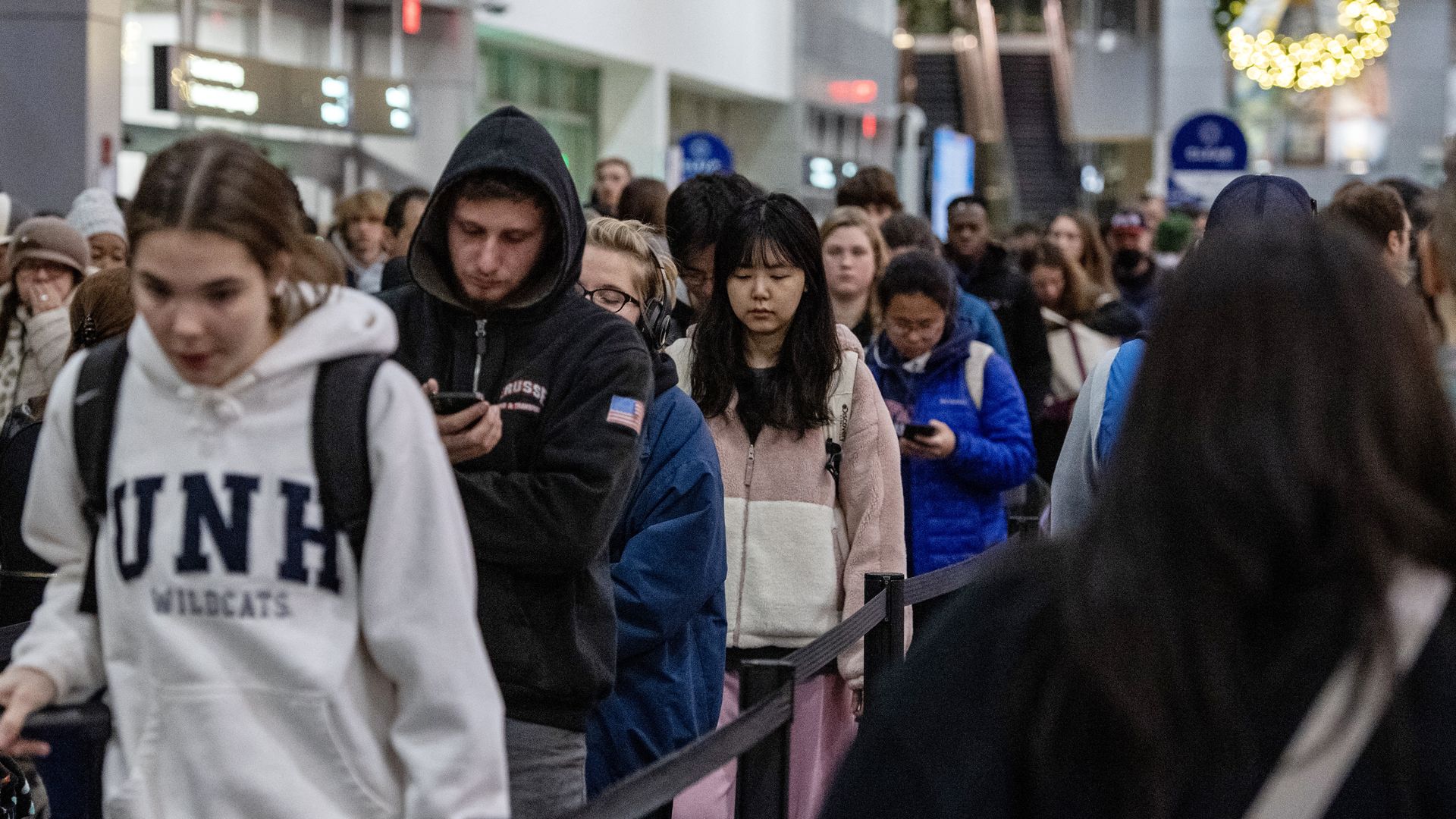 Alt text: Travelers wait in a long airport terminal line at Boston Logan.
