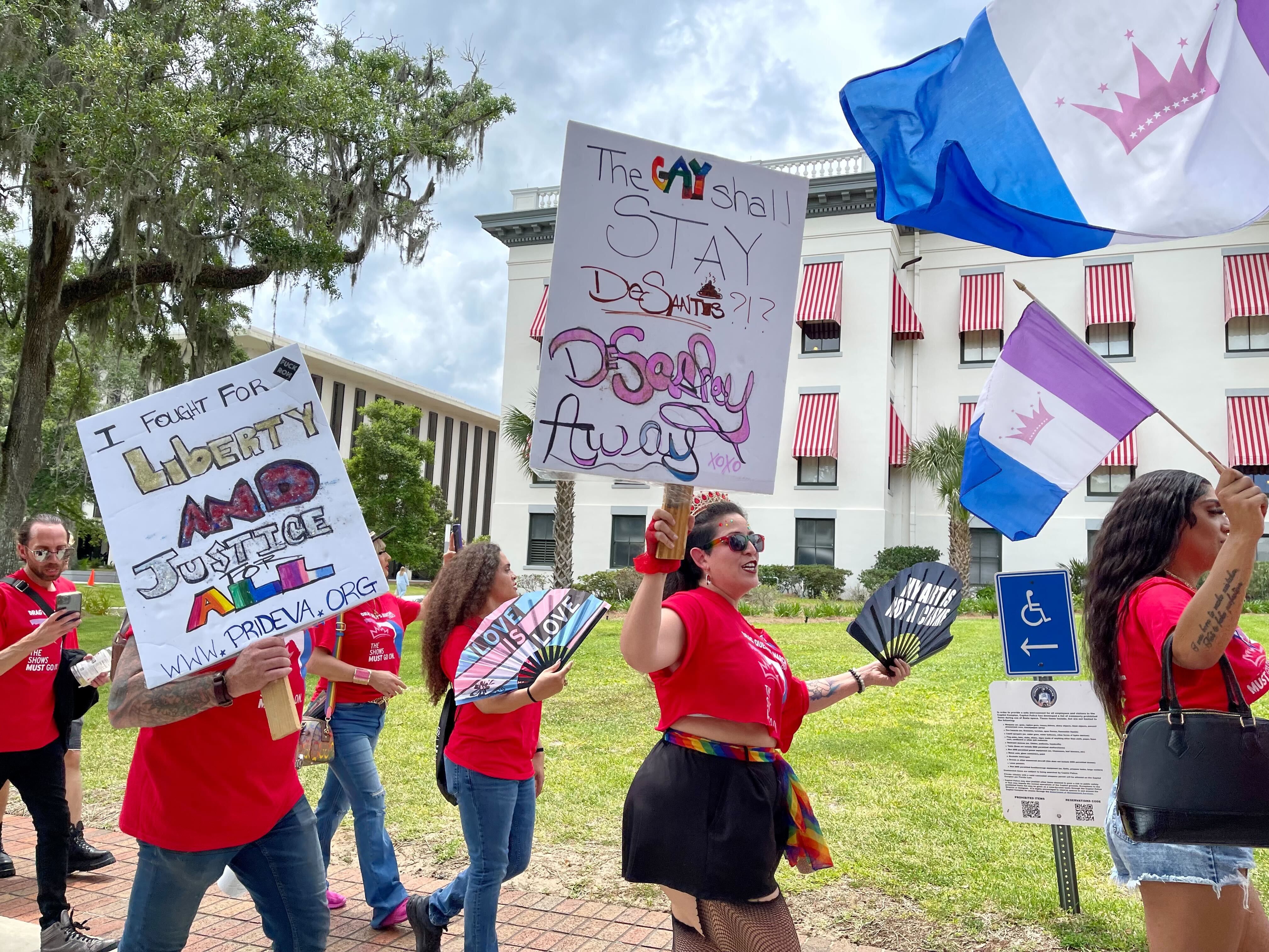 LGBTQ rights protesters wearing red shirts walk in a line with signs and flags.