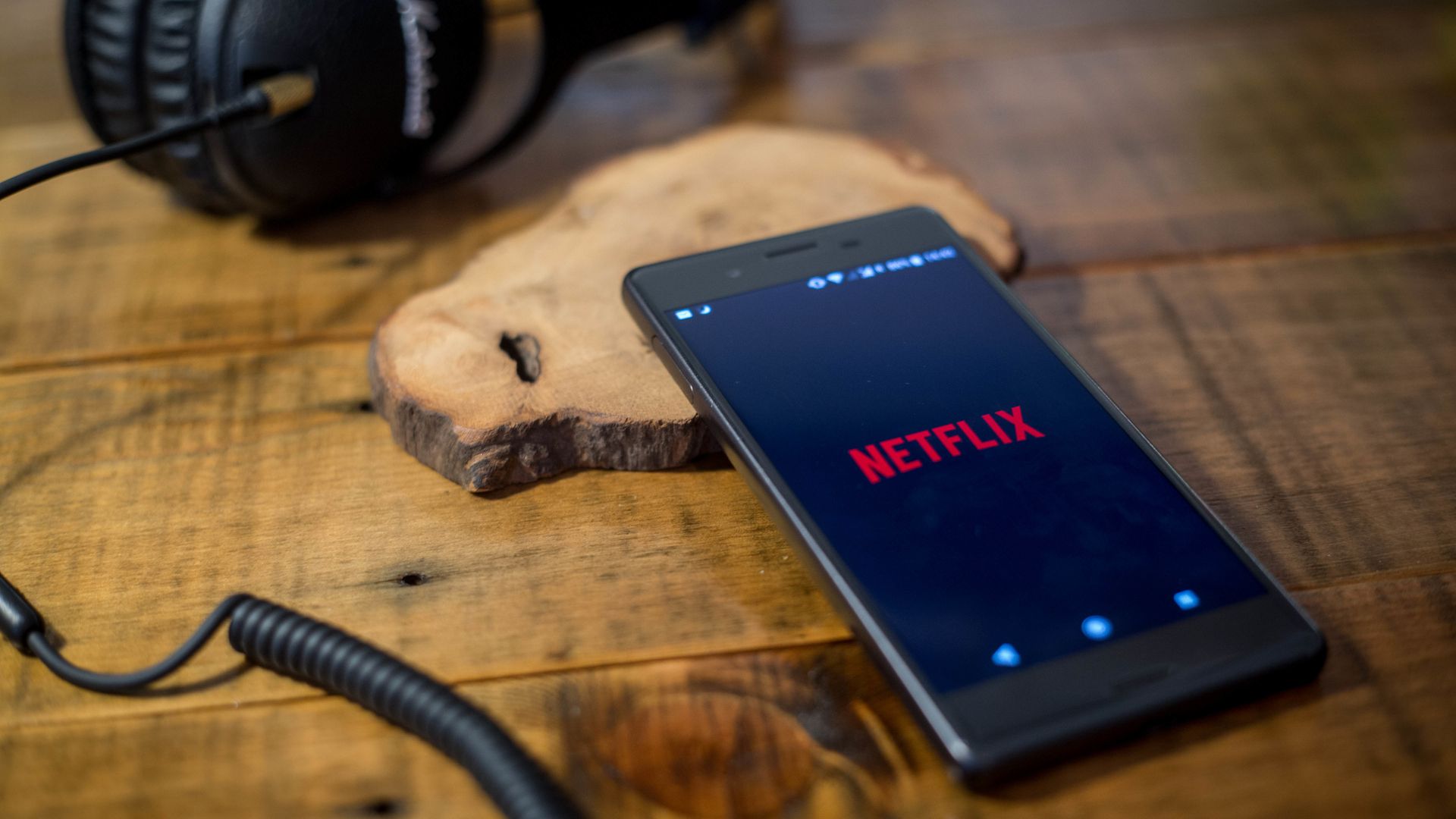 The netflix logo is displayed on a mobile phone with headphones plugged in 