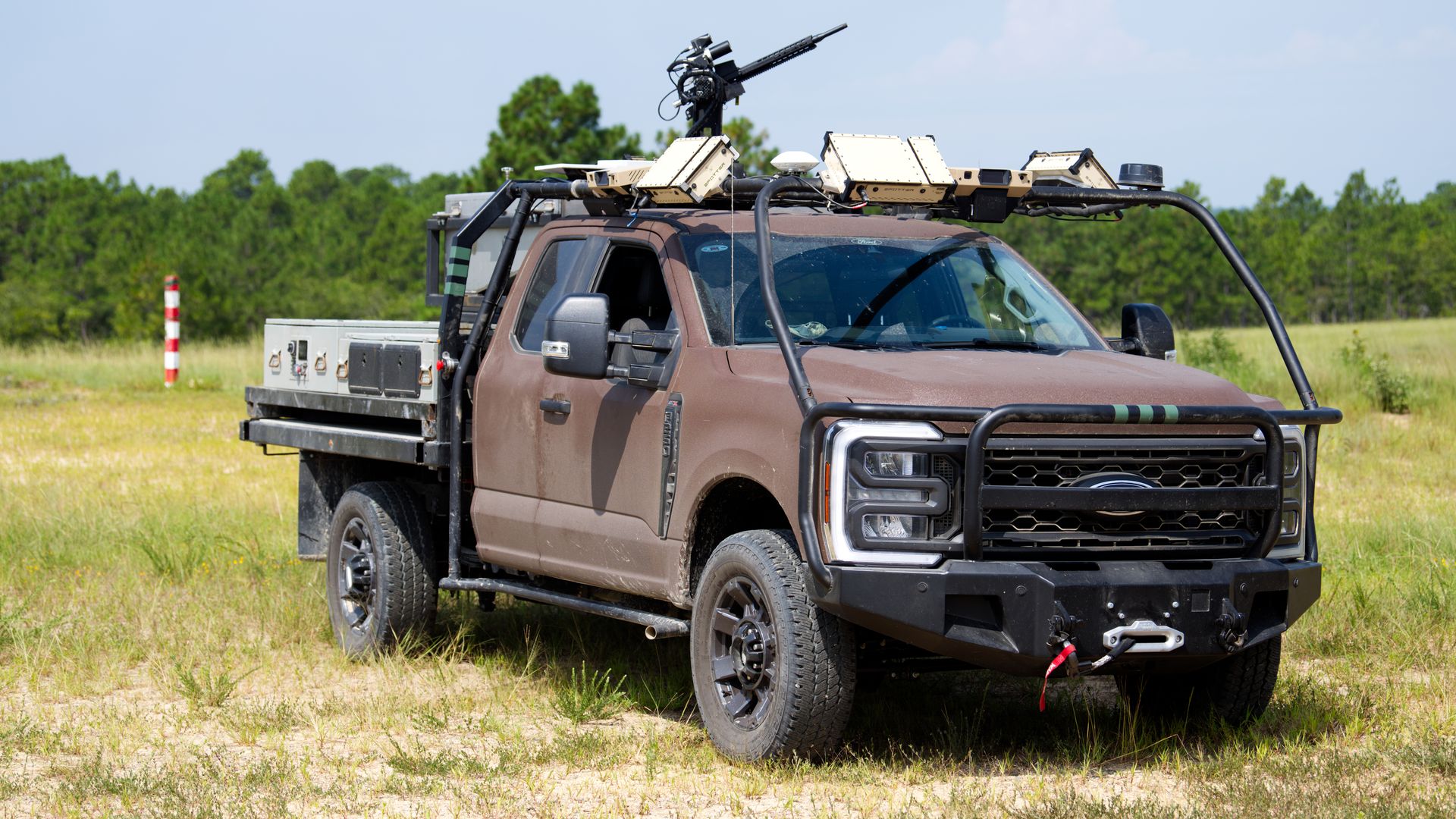 A ruggedized Ford F-250 sits in sandy hills. A gun turret can be seen on top of the truck.