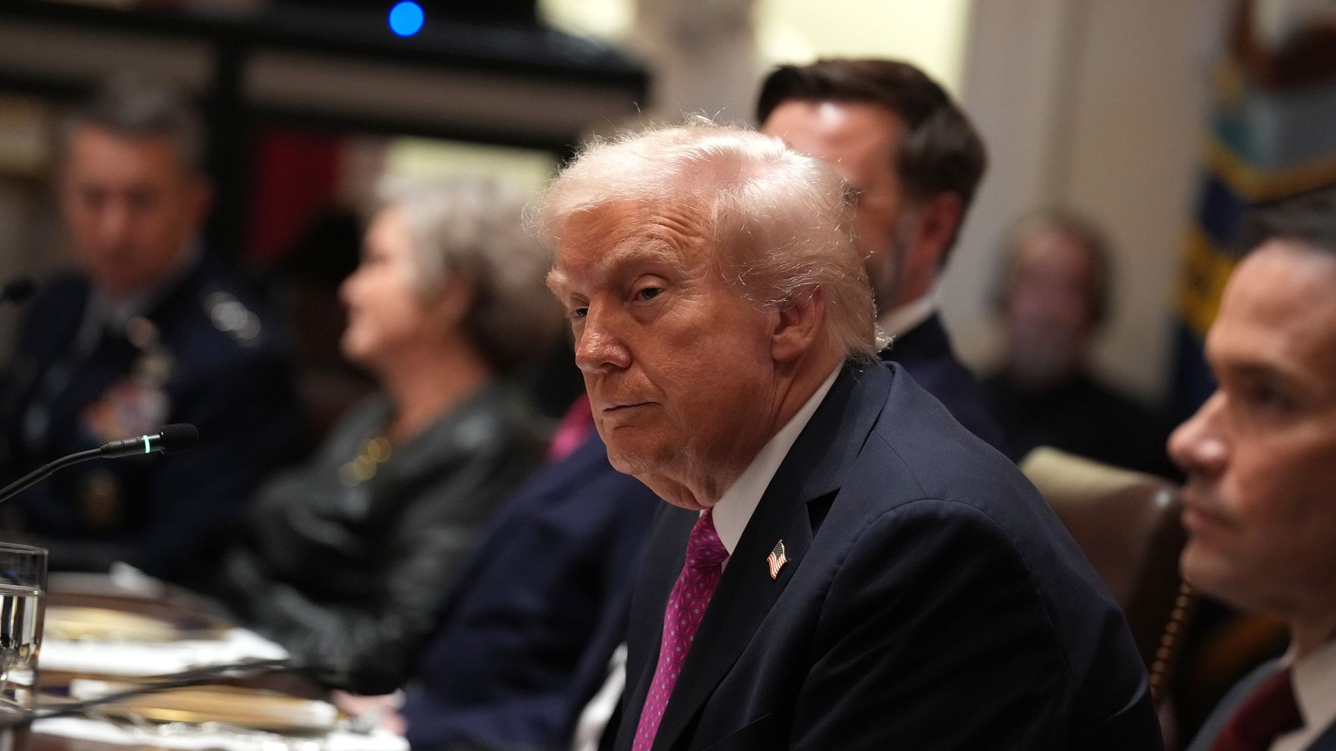 President Trump, wearing a navy jacket with a US flag pin at the top of his left lapel, white shirt and light red tie
