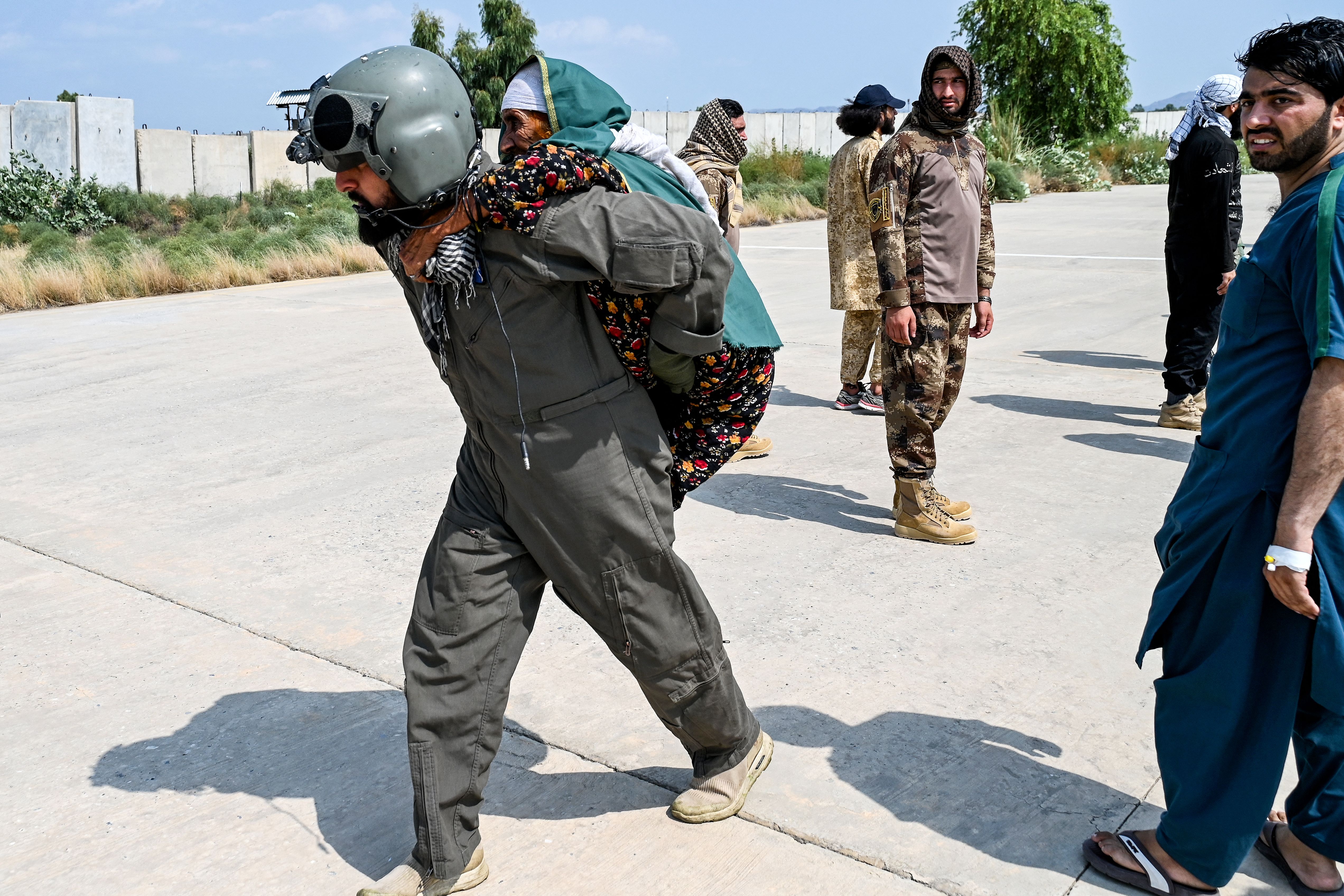 An Afghan military member carries an elderly earthquake victim in traditional dress of a green head scarf and floral dress.