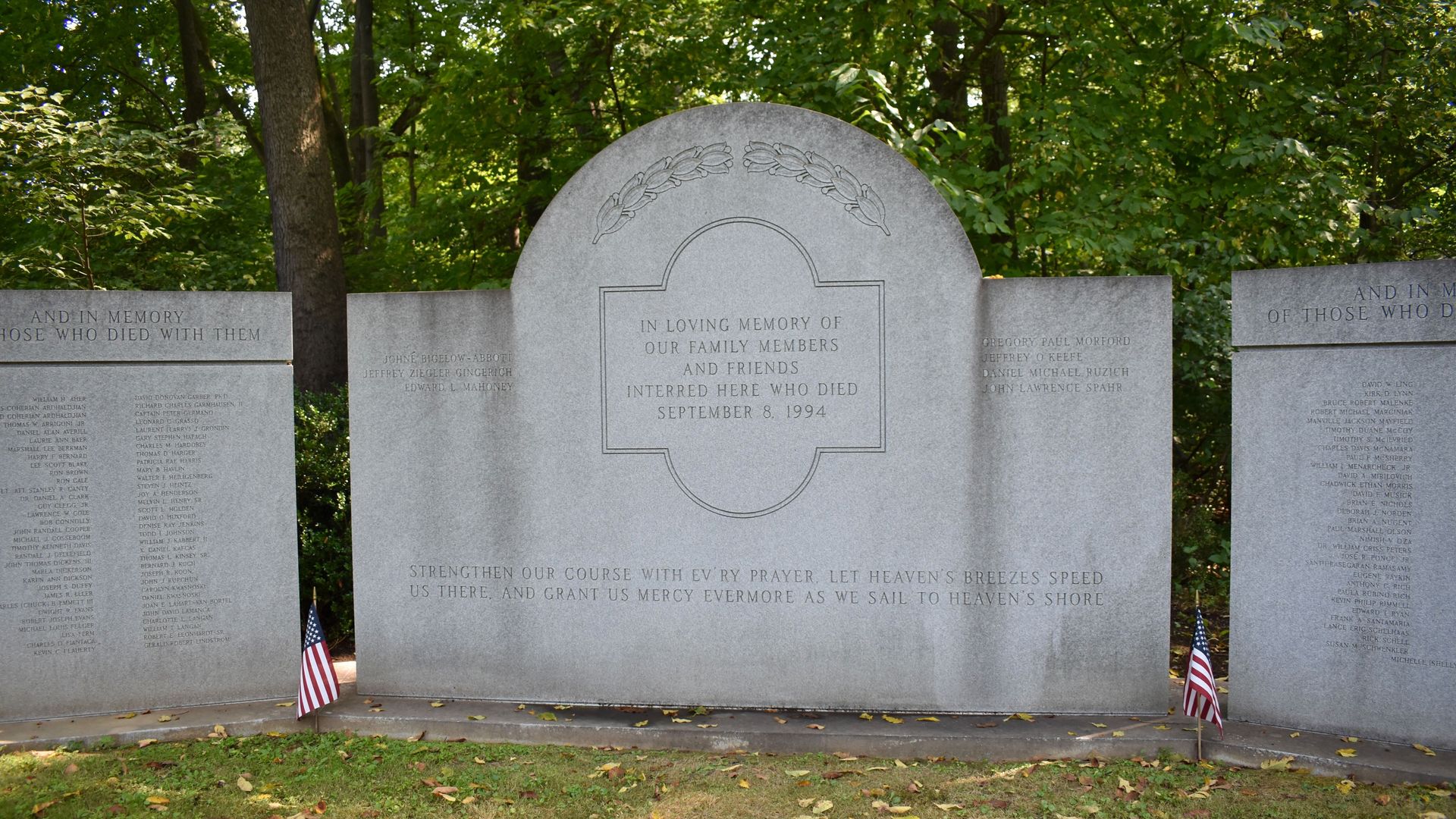 Gray stone memorial in a wooded area with engraved tribute to family and friends who died September 8, 1994, surrounded by names and two small American flags at its base.