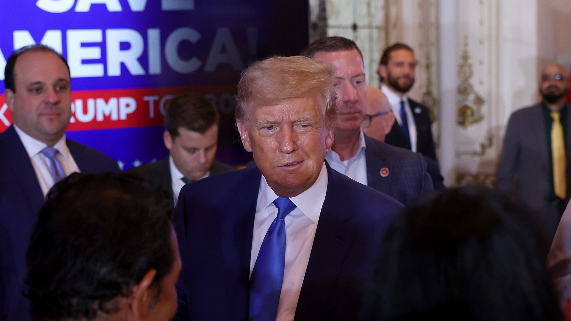 Former President Donald Trump, wearing a dark blue suit jacket, white shirt and blue tie, speaks to supporters in the opulent ballroom of his Mar-a-Lago resort in Palm Beach, Florida.