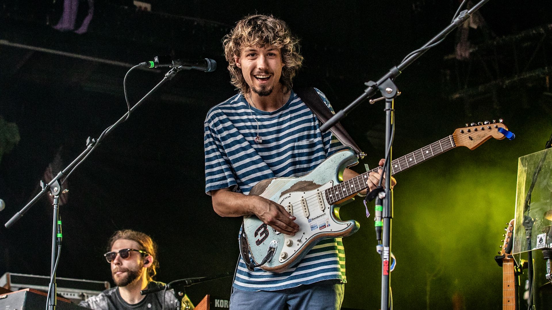 A man playing electric guitar on stage with his band behind him.