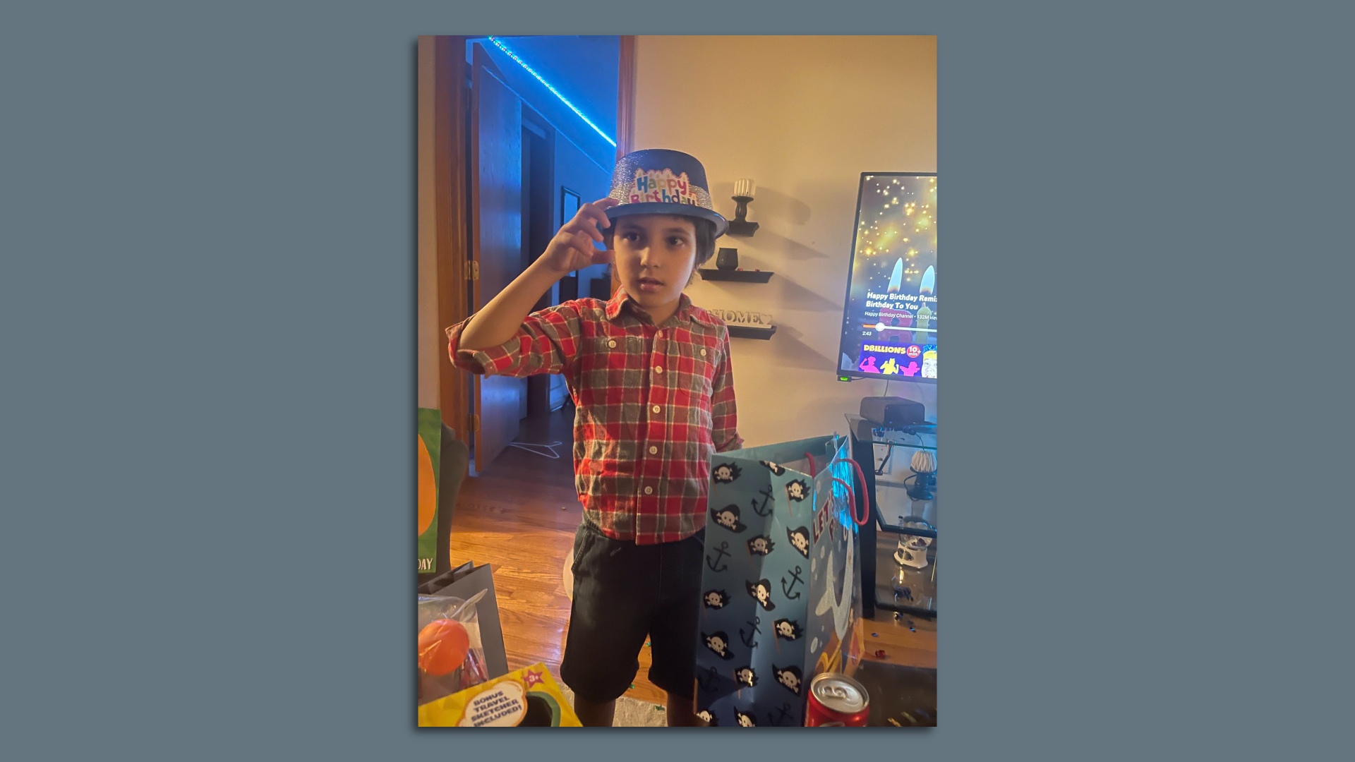 Wadea Al-Fayoume, 6, wears a hat that says "happy birthday" and holds a gift bag inside a home.