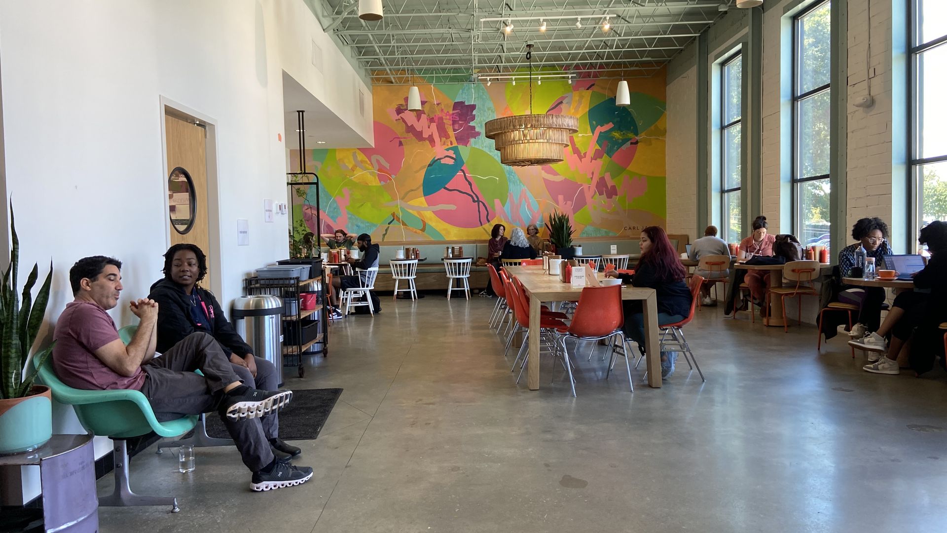 People talk, work and eat in a large coffee shop with a bright mural on the back wall