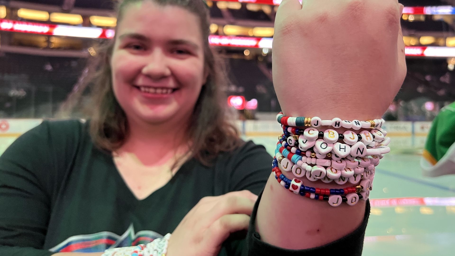 A woman in a black v-neck with a Columbus Blue Jackets logo holds up a wrist full of friendship bracelets reading "Johnny Hockey"