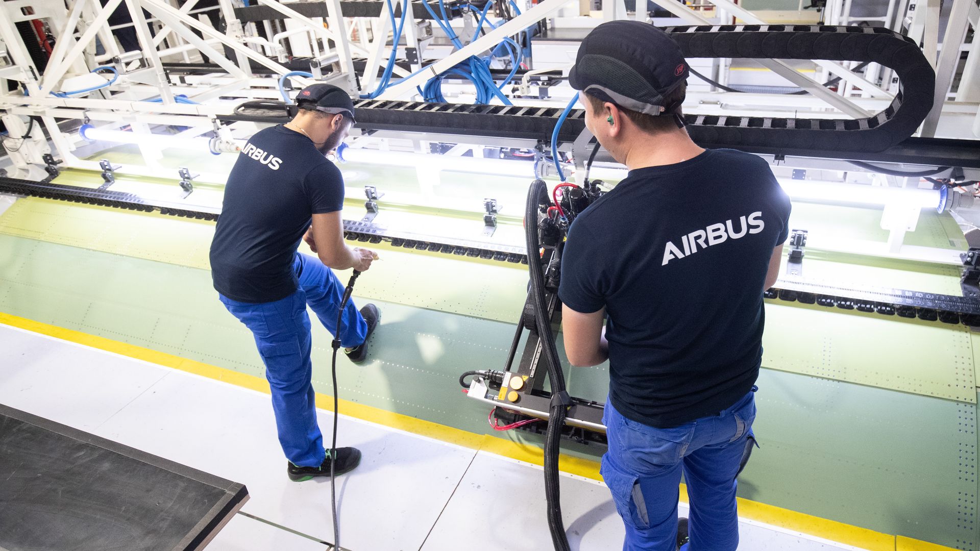 In this image, two men wearing shirts with the Airbus logo work on assembling an Airbus plane