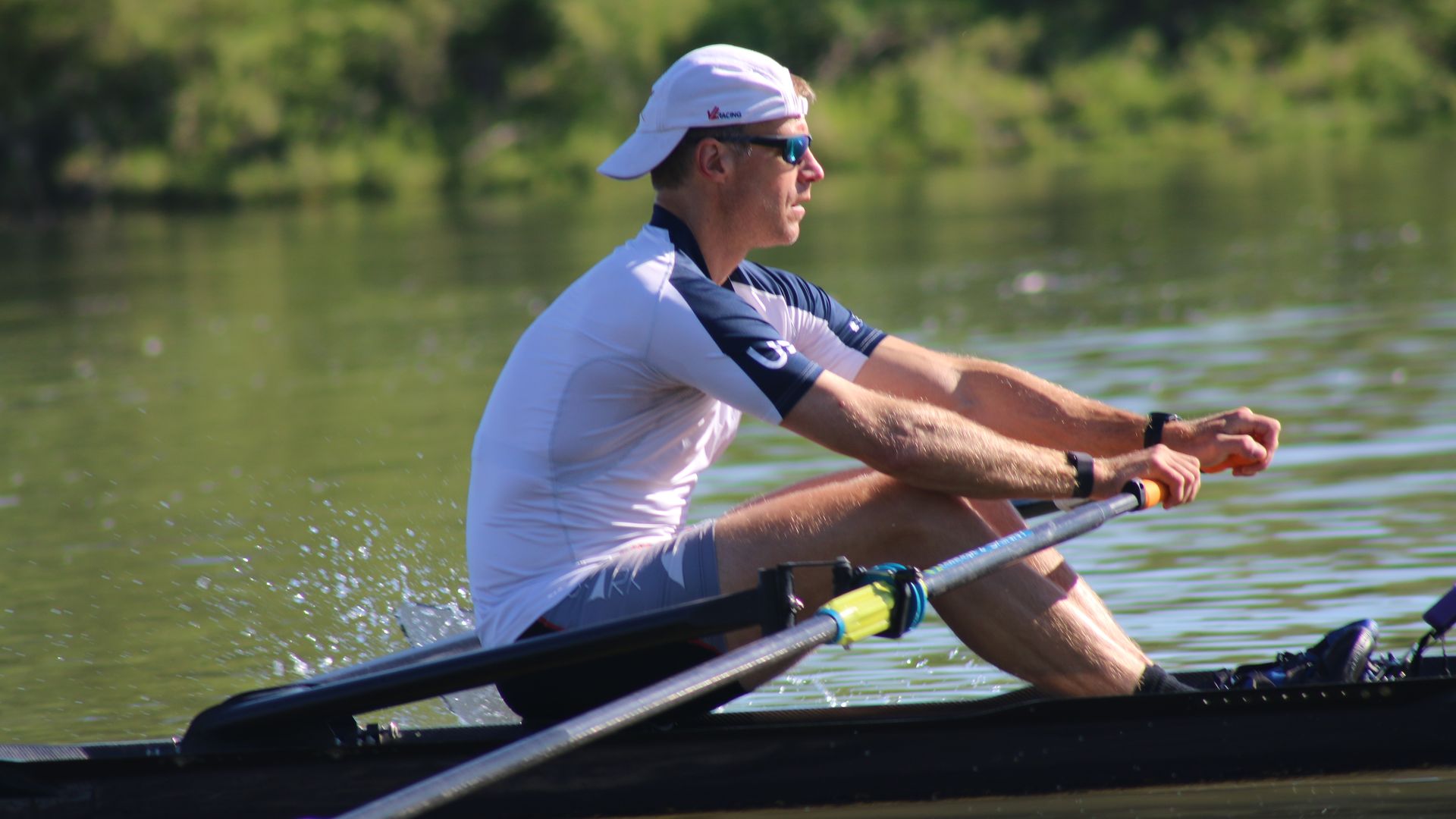 A photo of a person sitting in a rowing boat and holding the oars with their two hands.