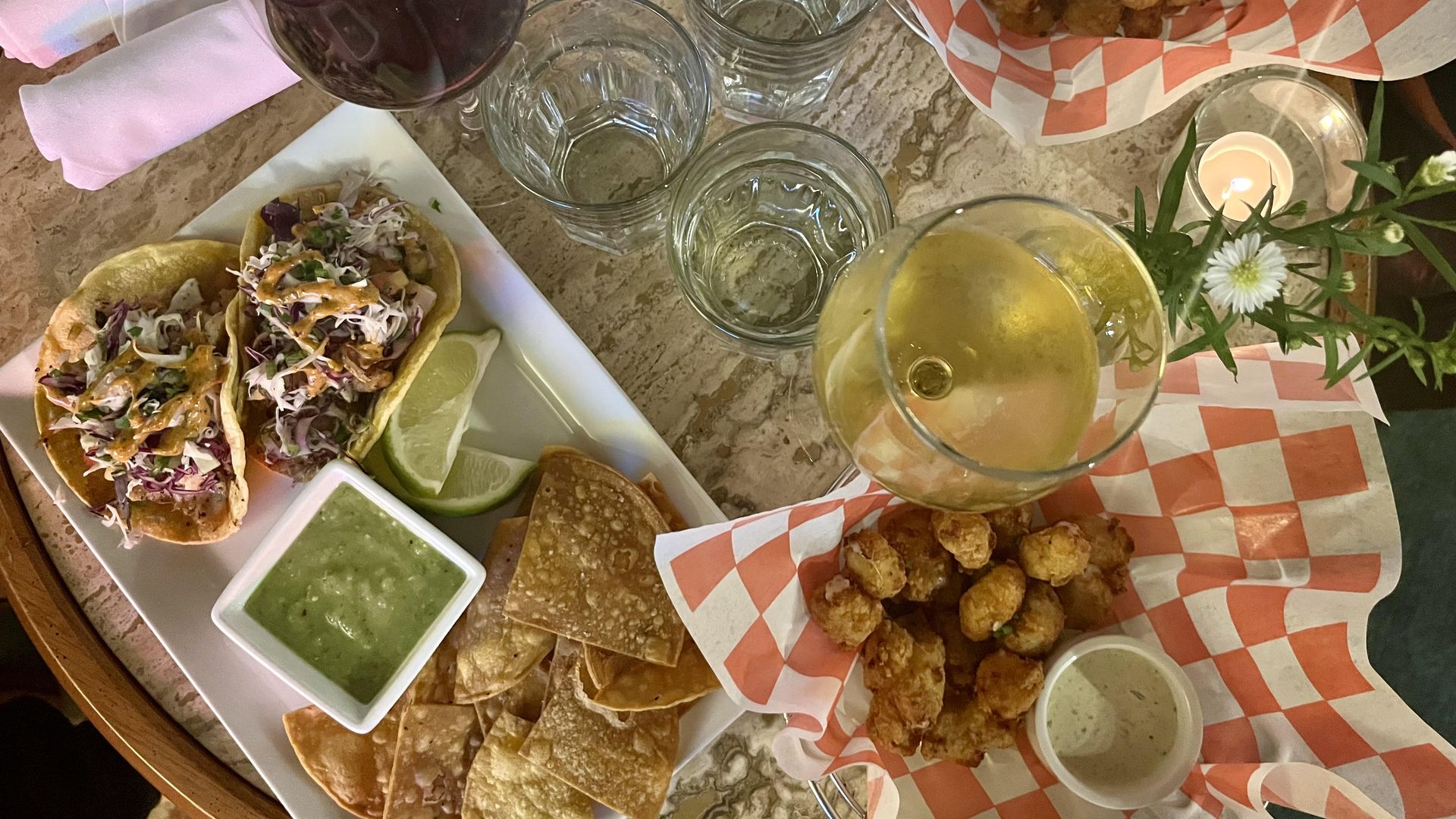 A table with red and white wine glasses, a plate with fish tacos and chips, and two baskets full of fried cheese curds.