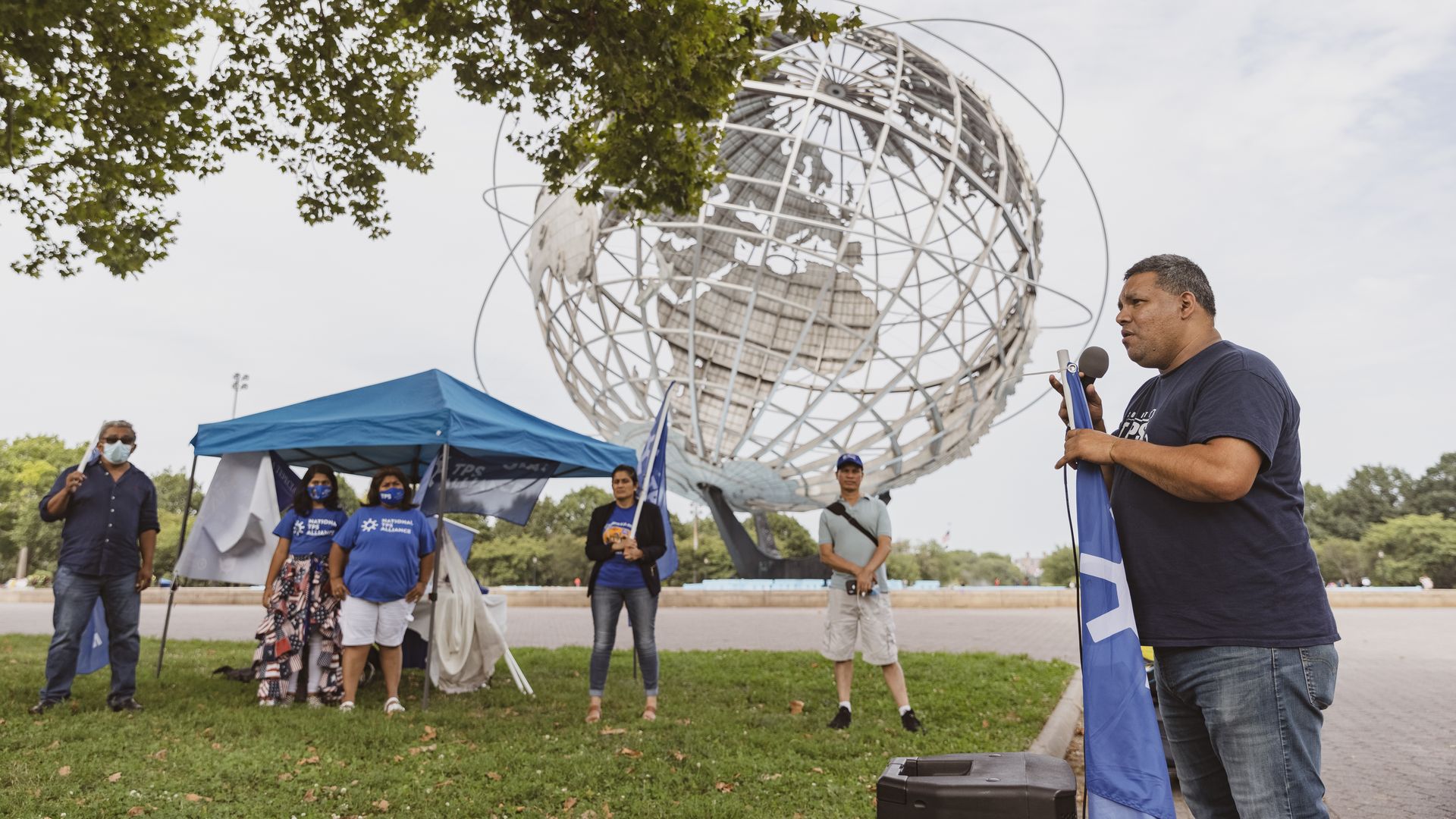 Josè Palma, a TPS holder from El Salvador (right), speaks into a microphone while holding the National TPS Alliance's blue flag during a rally in New York City in 2021.