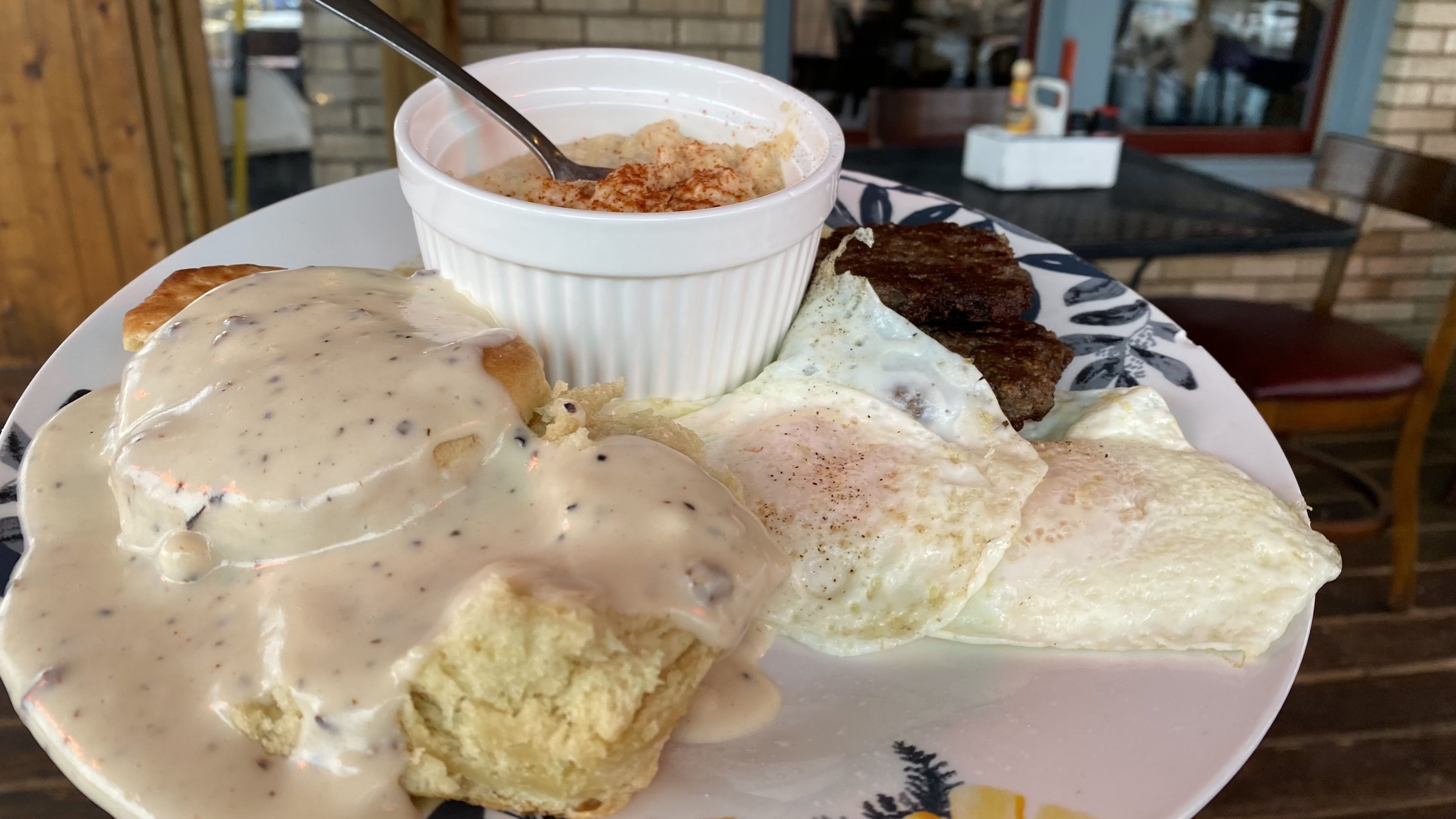 A plate of eggs, sausage, grits and a biscuit with gravy.