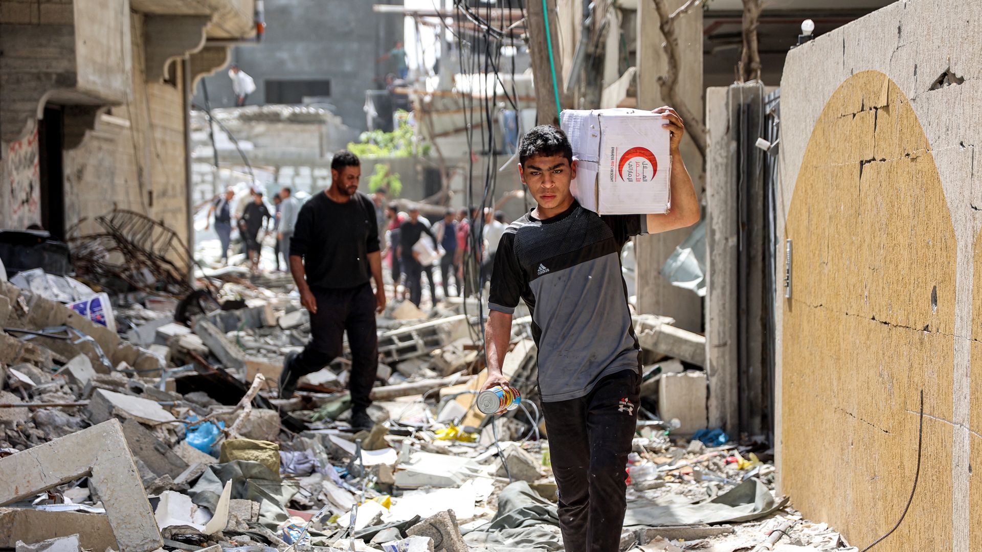 People walk through rubble past damaged buildings with one of the humanitarian aid packages collected from a drop over the northern Gaza Strip on April 23, 2024 