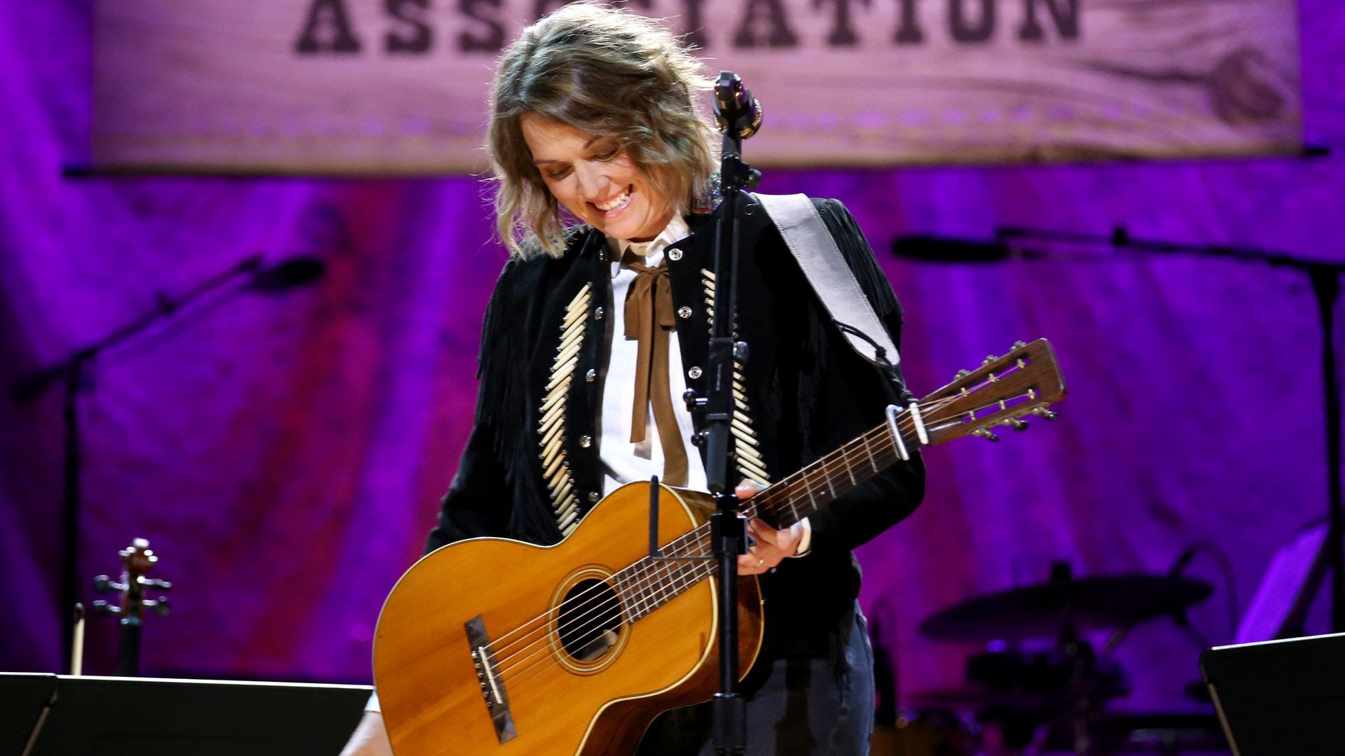 Brandi Carlisle holding a guitar and performing at the 2019 Americana Awards.