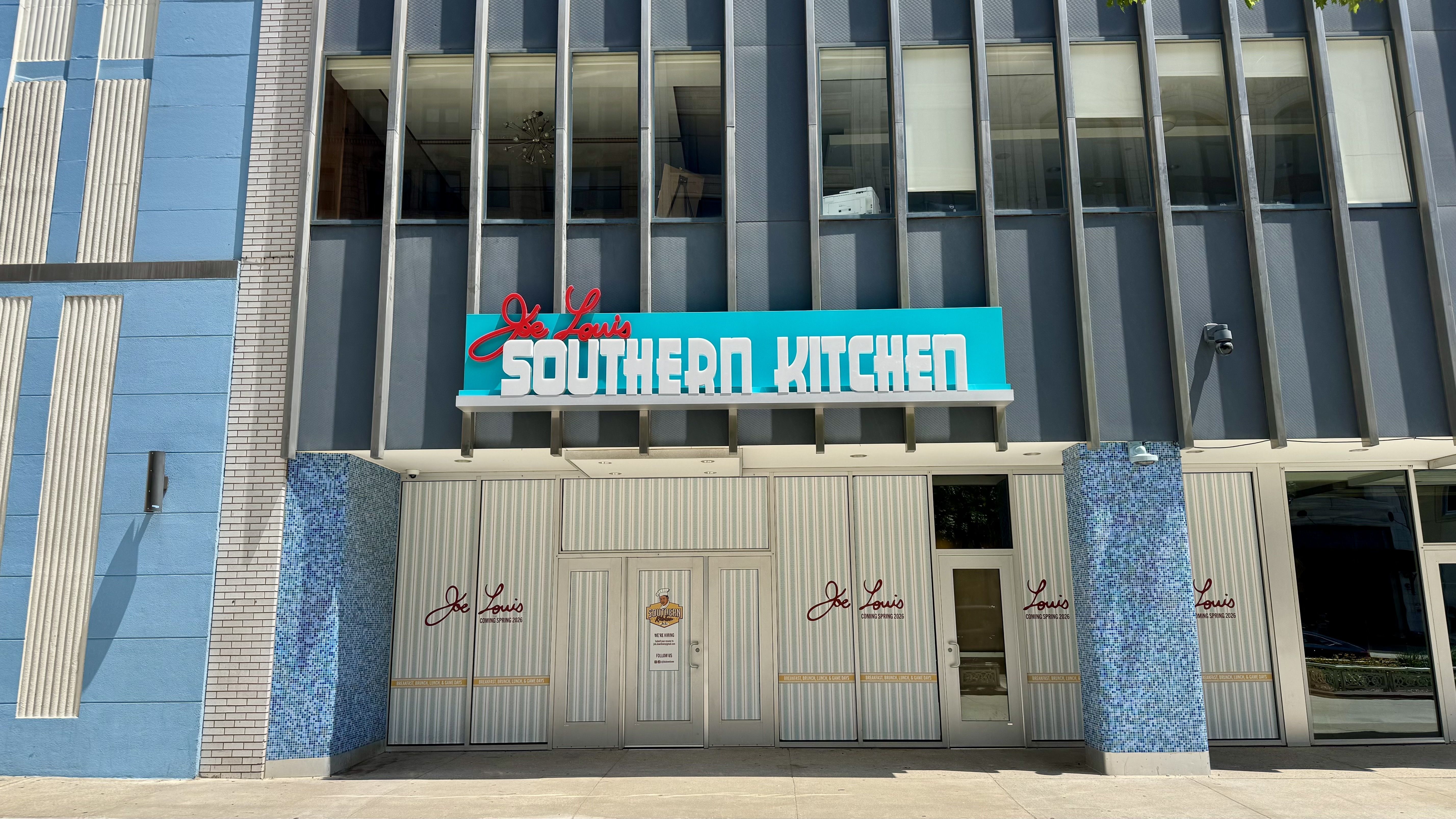 Front of a blue modern building with tall vertical metal frames and large glass windows; turquoise sign reads "JOE LOUIS SOUTHERN KITCHEN" above the entrance.