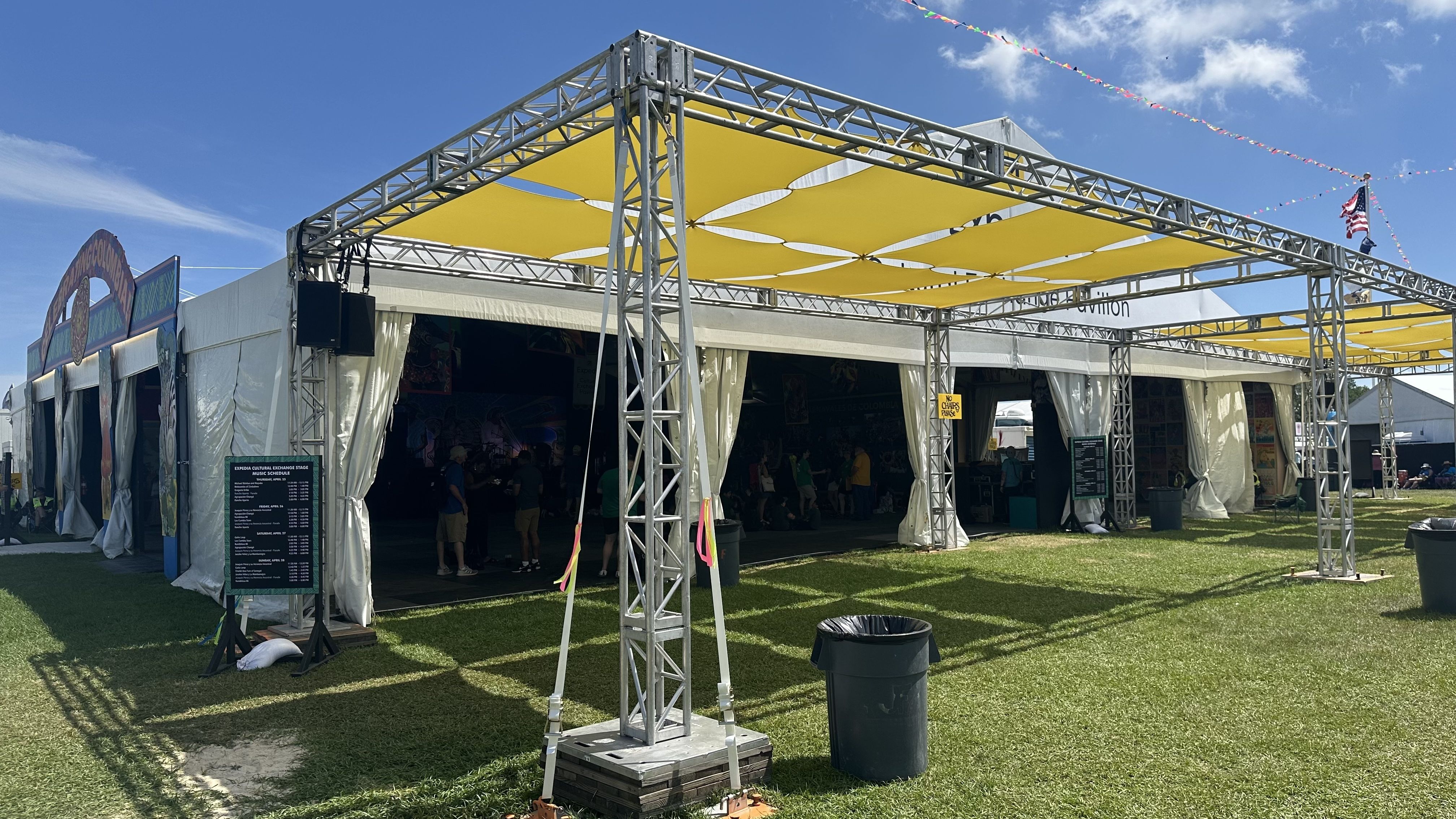 Metal scaffolding with yellow sunshades atop it sits adjacent to a white festival tent.