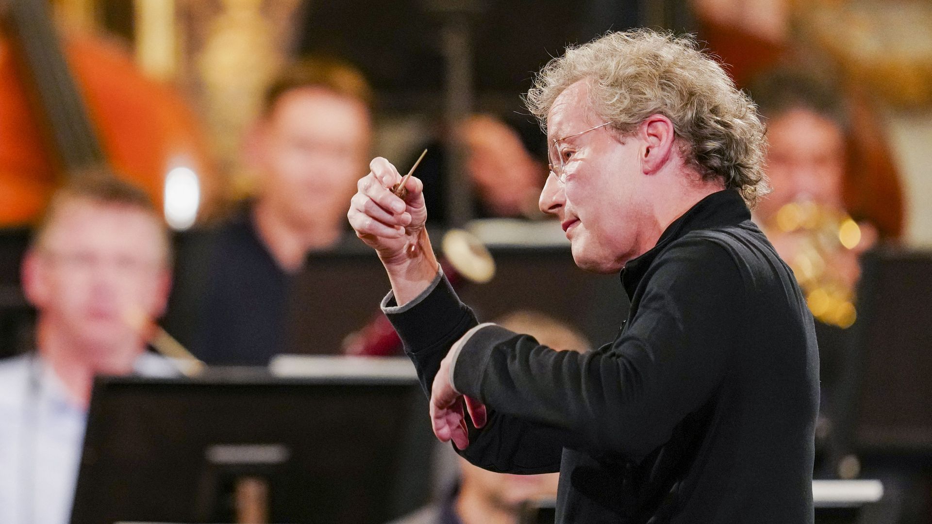 Man with curly gray hair in profile conducting an orchestra