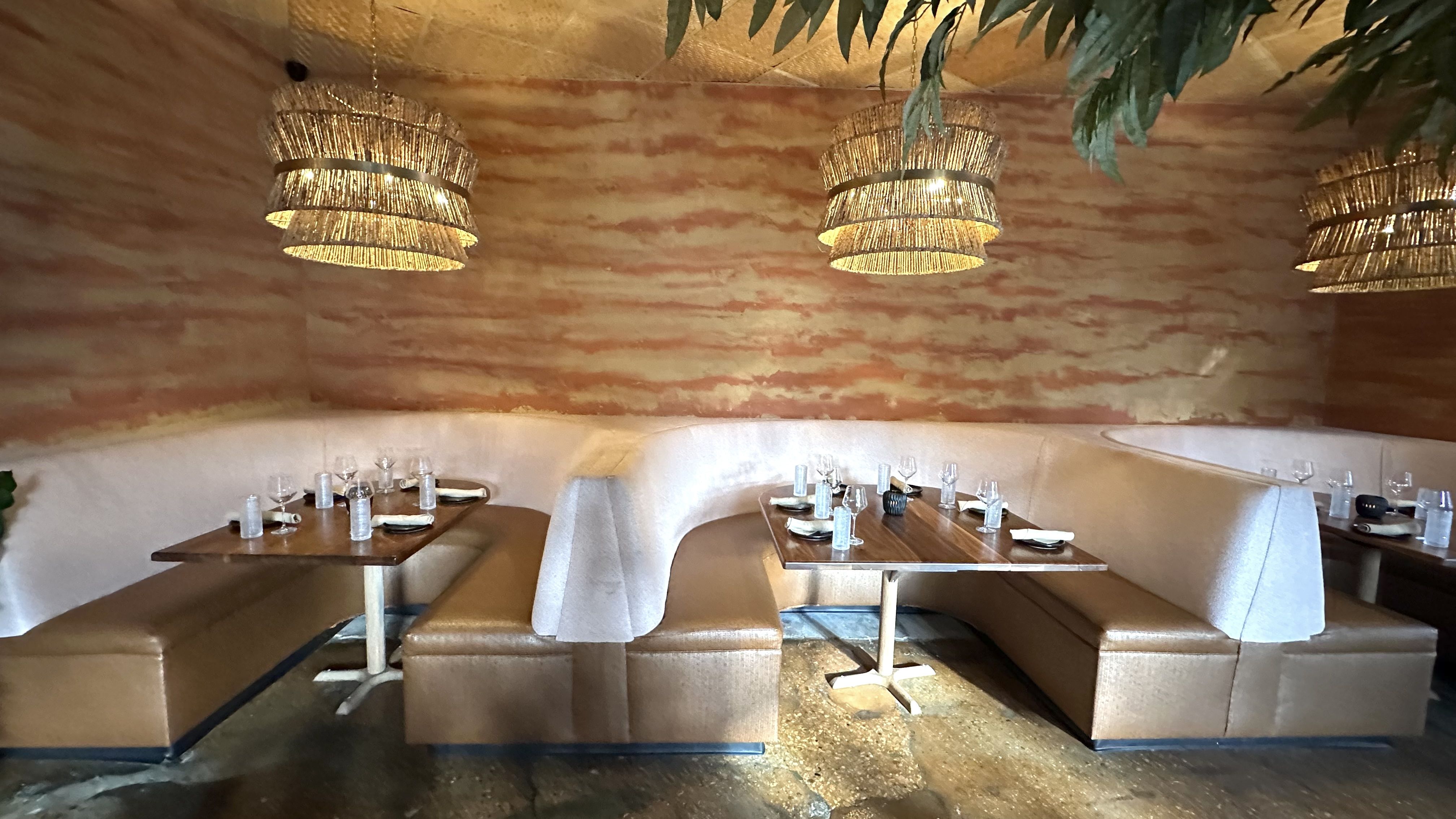 A trio of curved booths is against a wall with rattan pendant lights hanging over each.