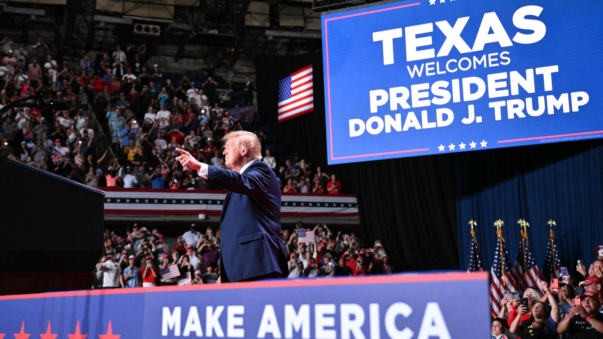 President Trump greets supporters at a rally at the Freeman Coliseum in San Antonio on Wednesday. A blue sign in the background reads "Texas welcomes President Donald J. Trump." A blue sign below Trump reads "Make America Great Again!" A crowd claps in the background as Trump points.
