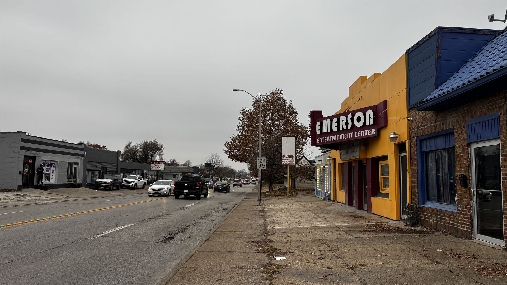 Street view with several cars and trucks, gray sky overhead, and a brightly colored yellow and red Emerson Entertainment Center on the right, along with other buildings and signs.