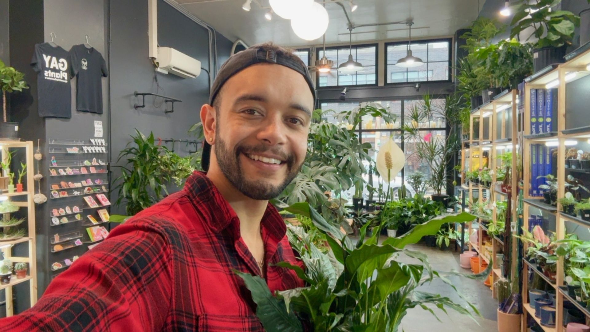 A pic of a man in a red flannel plaid shirt in a store filled with plants.