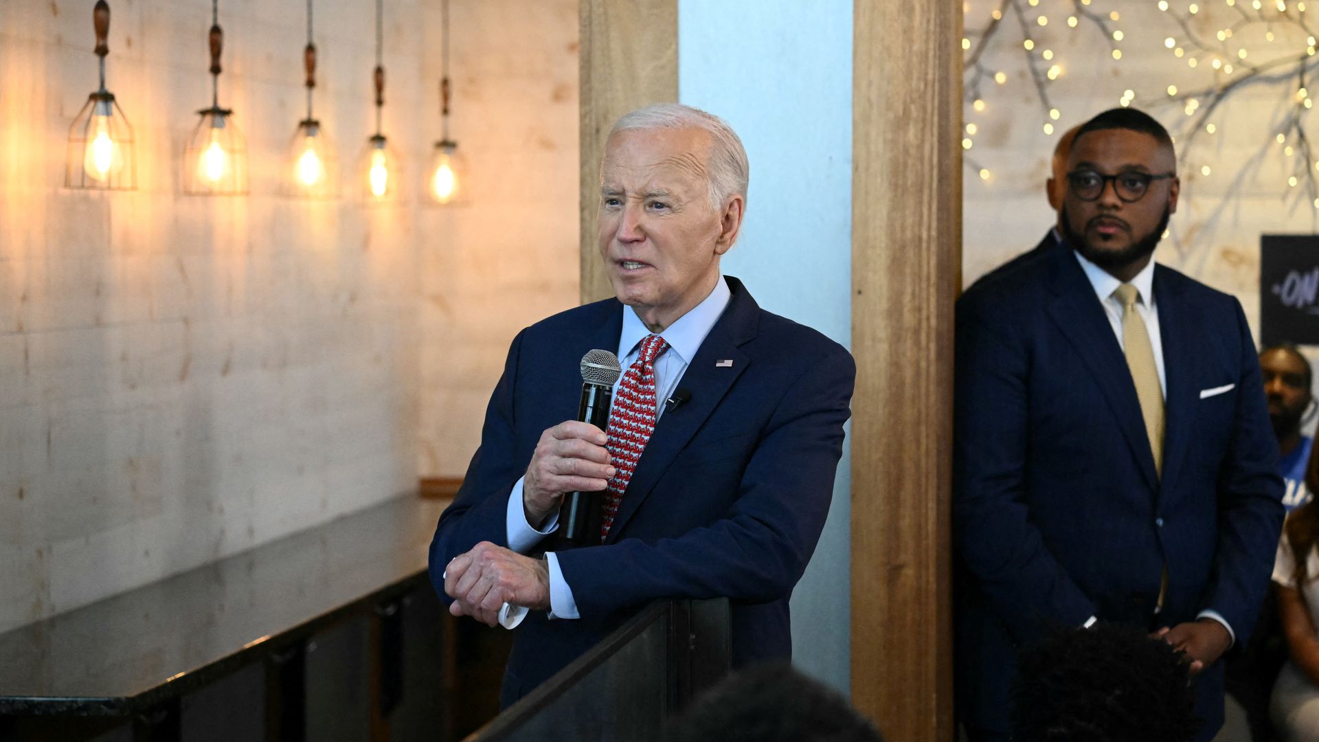 President Biden, wearing a blue suit and speaking into a microphone at a campaign event.