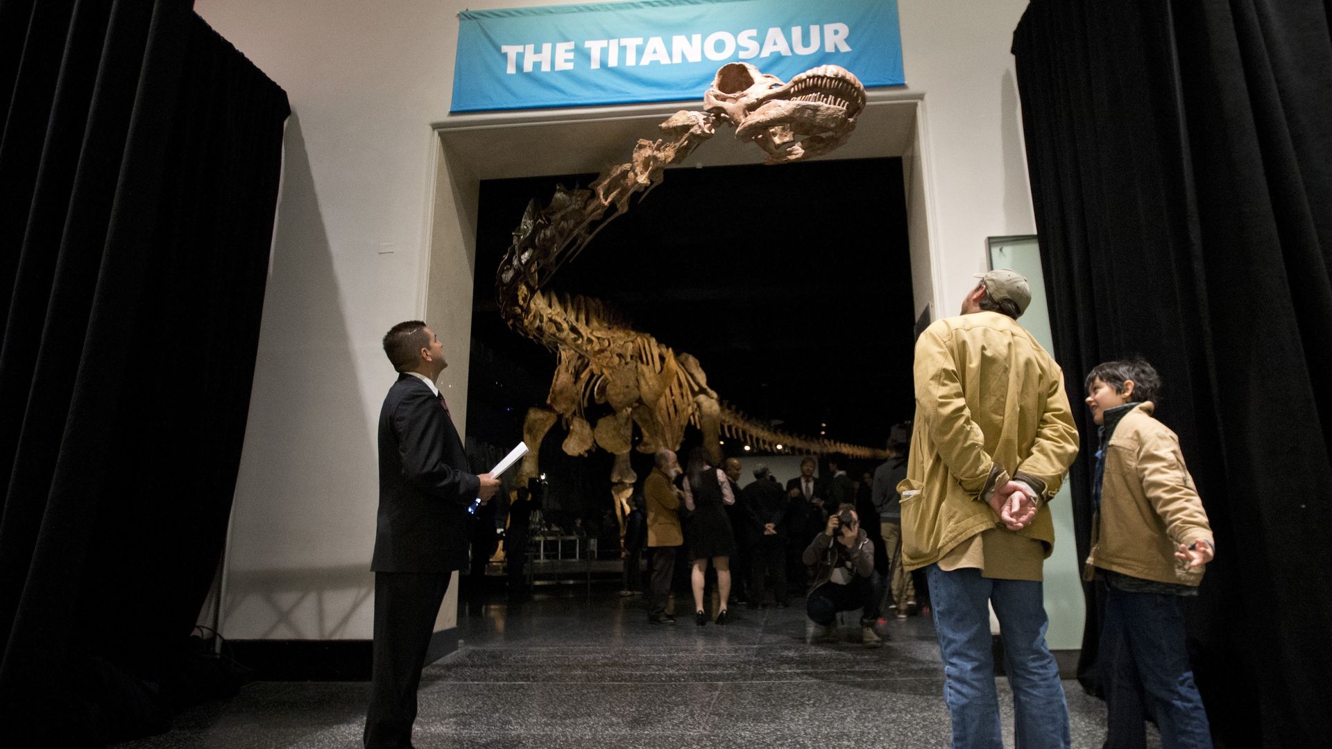 Visitors to the American Museum of Natural History examining a replica of a 122-foot-long dinosaur on display.