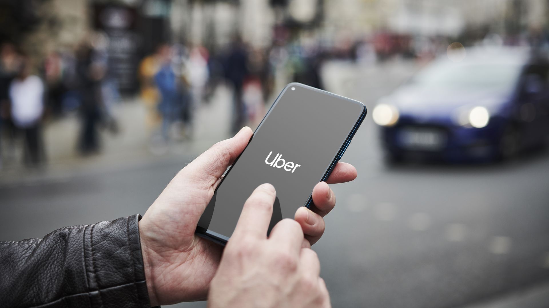 Detail of a man holding up an Honor 20 Pro smartphone with the Uber transport app visible on screen, while taxis queue in the background