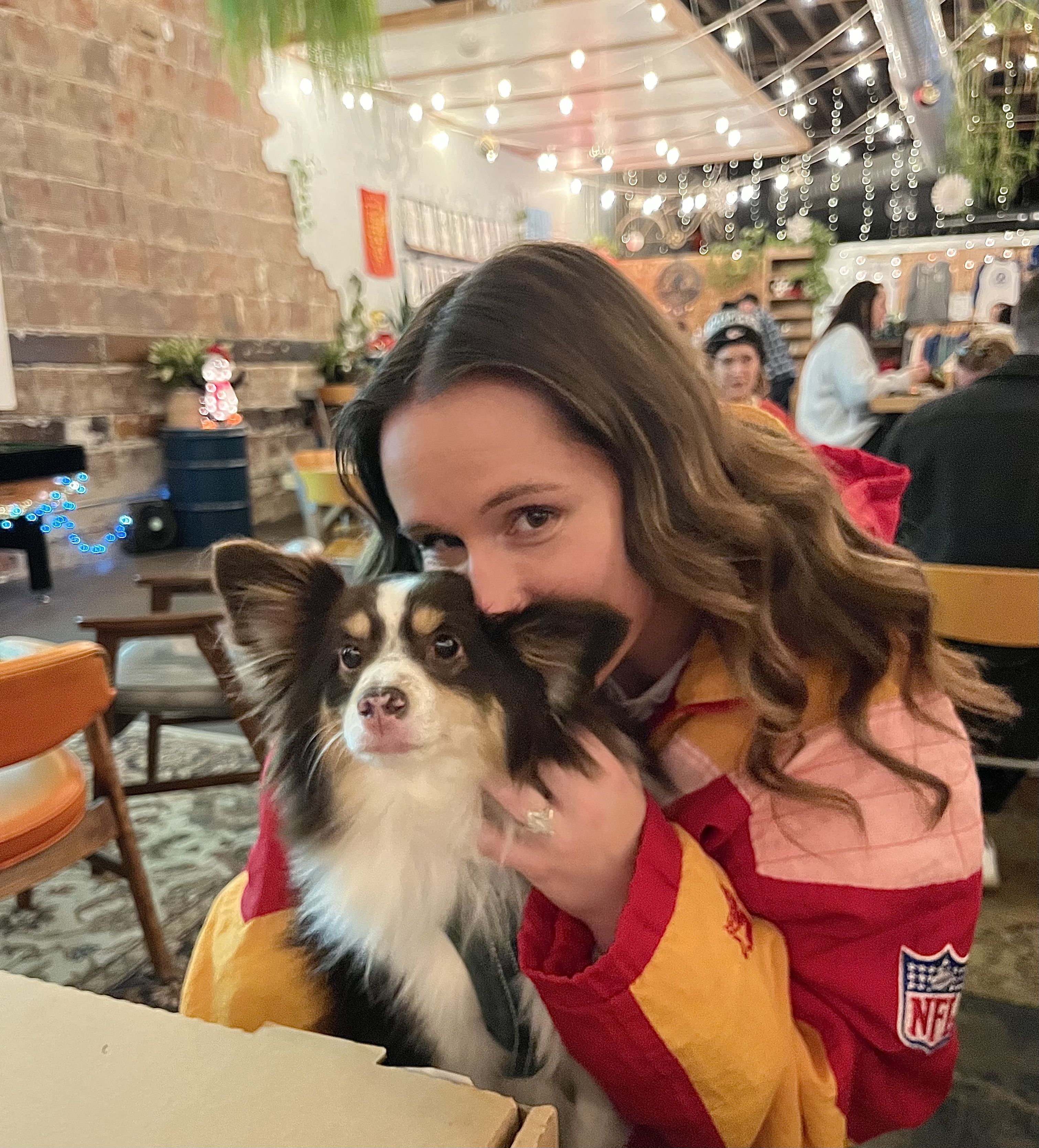 Photo of Ollie and a woman at Casual Animal with twinkle lights in the background and a pizza box in the foreground.