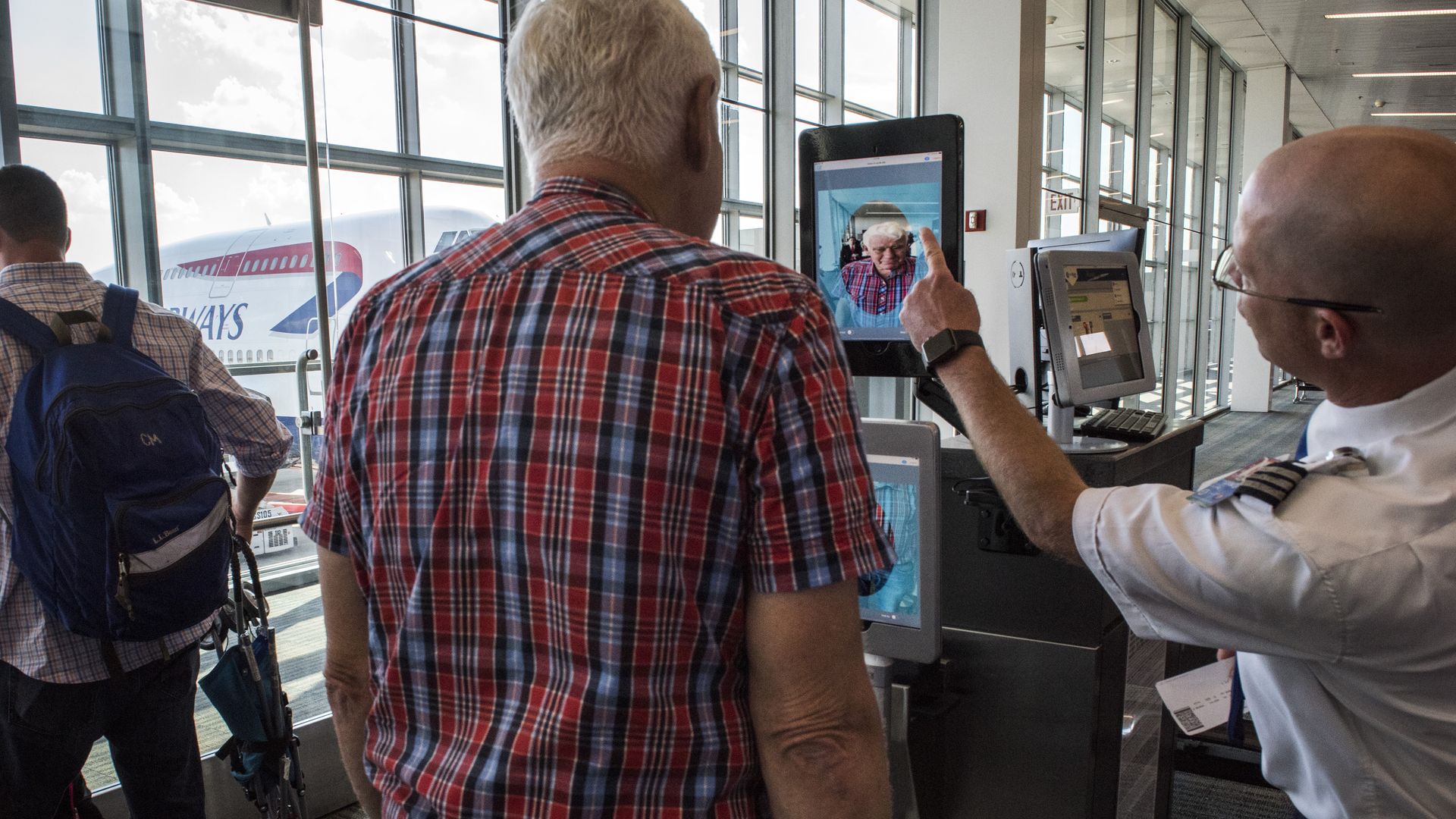 A man looks into a tablet showing his own face as another man points to it