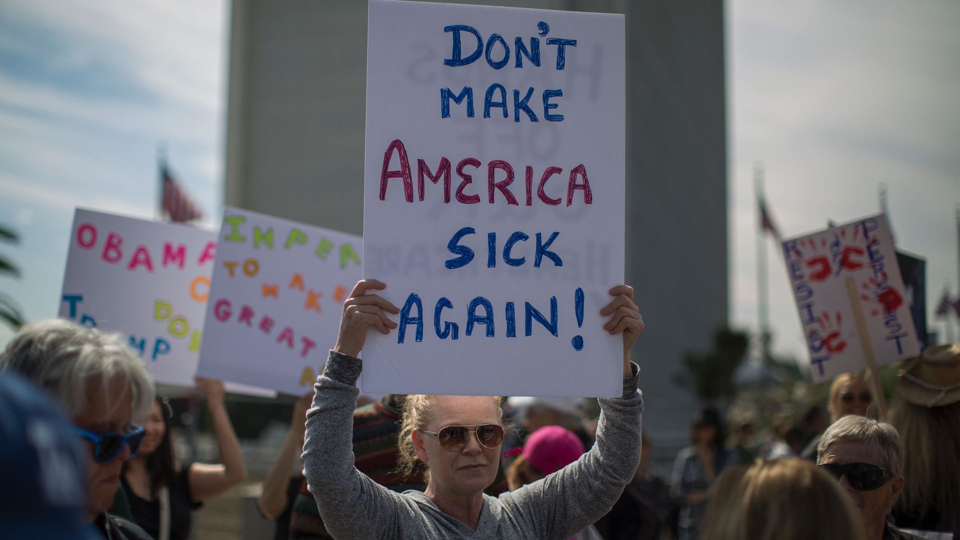A woman holds a sign that reads, "Don't make America sick again!"