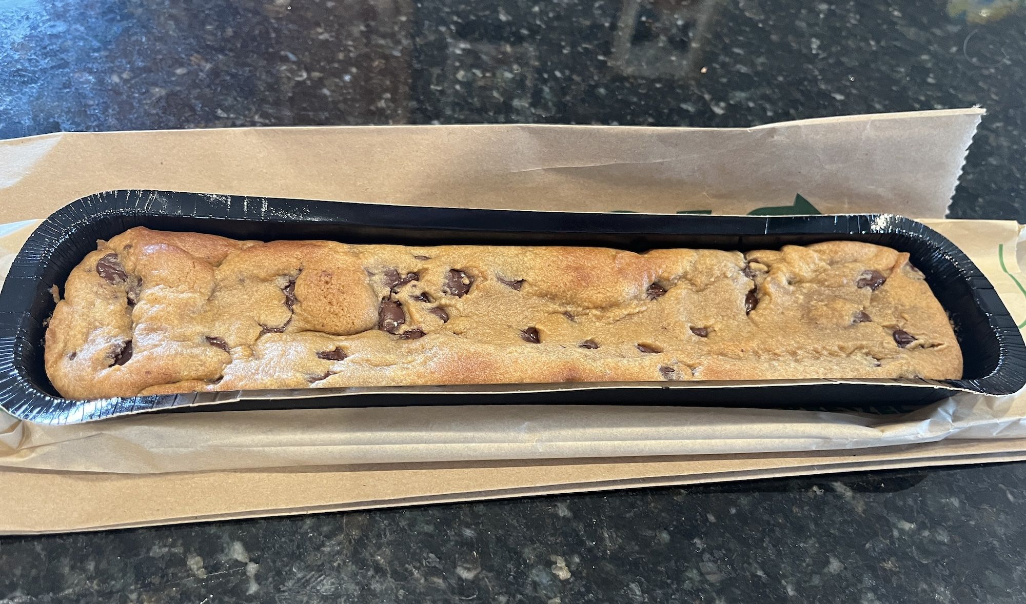 Foot-long chocolate chip cookie in black plastic tray.