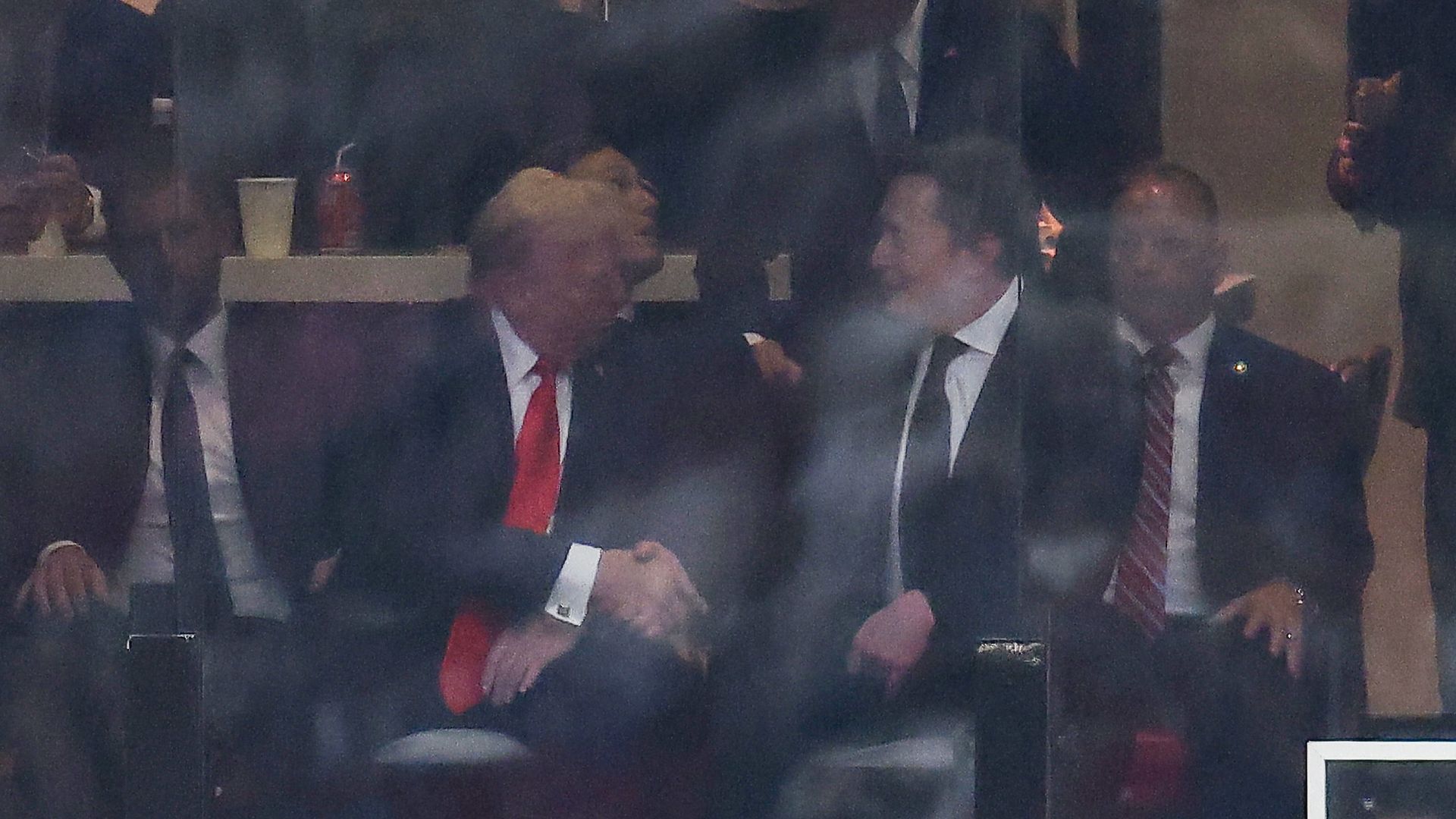 President Trump, wearing a black jacket, white shirt and red tie, and Tesla CEO Elon Musk, wearing a black suit, white shirt and black tie, shaking hands at Charlie Kirk's memorial service.