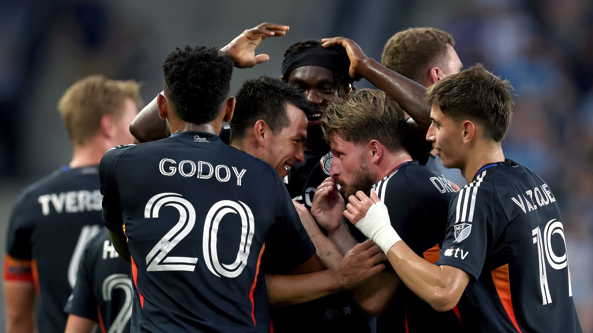 A group of five San Diego FC players huddle and hug in celebration after a goal. 
