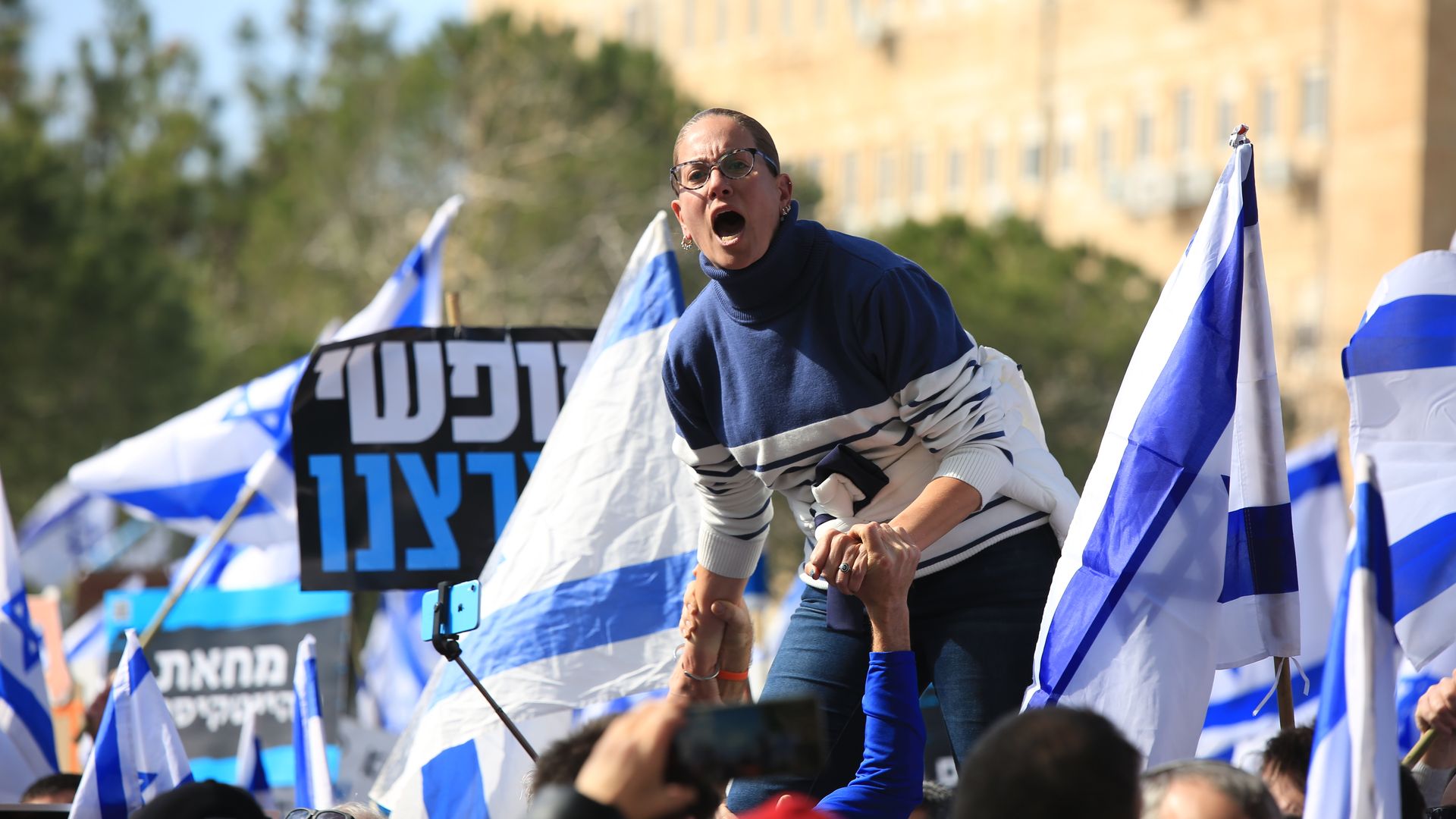 Israeli people, holding flags, gather in front of the parliament building (Knesset) to stage a demonstration against judicial reform plans during a preliminary vote in Jerusalem on February 13, 2023