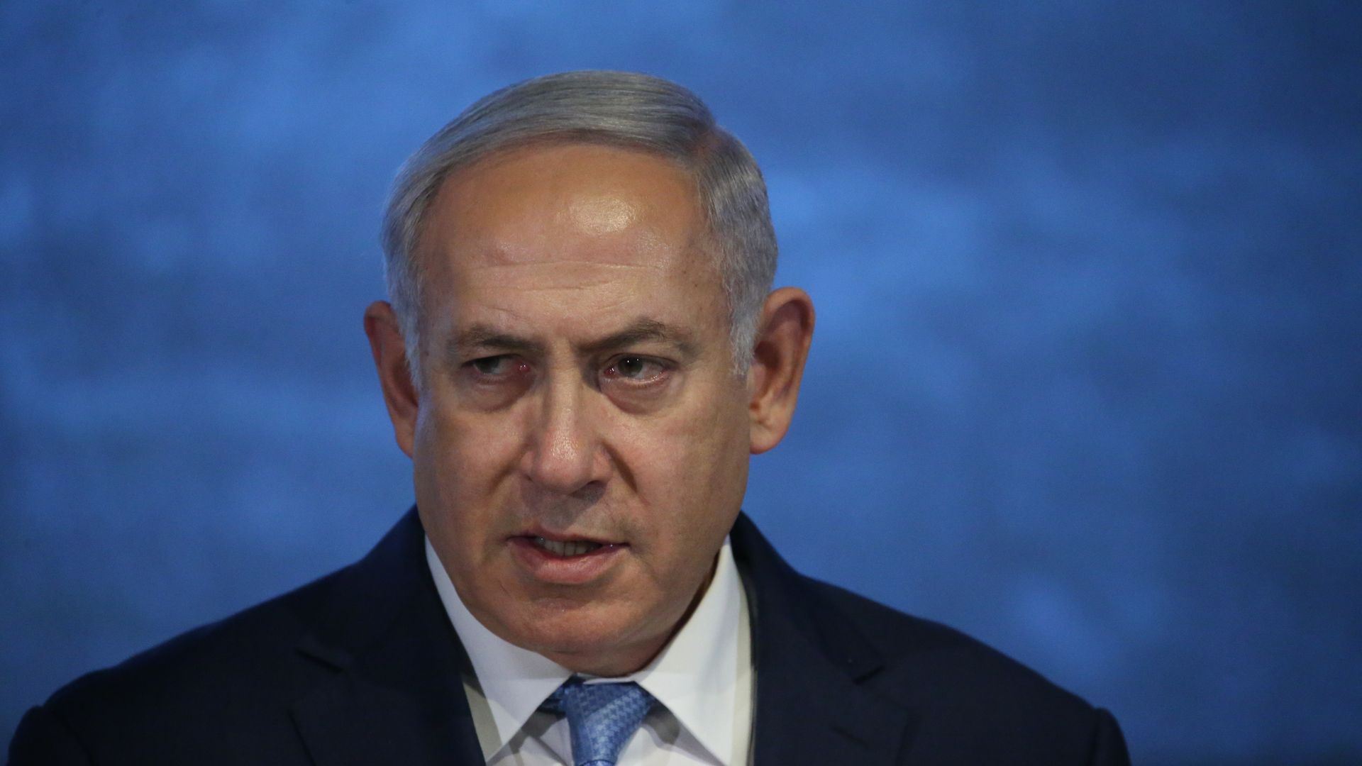 Benjamin Netanyahu before a blue backdrop.