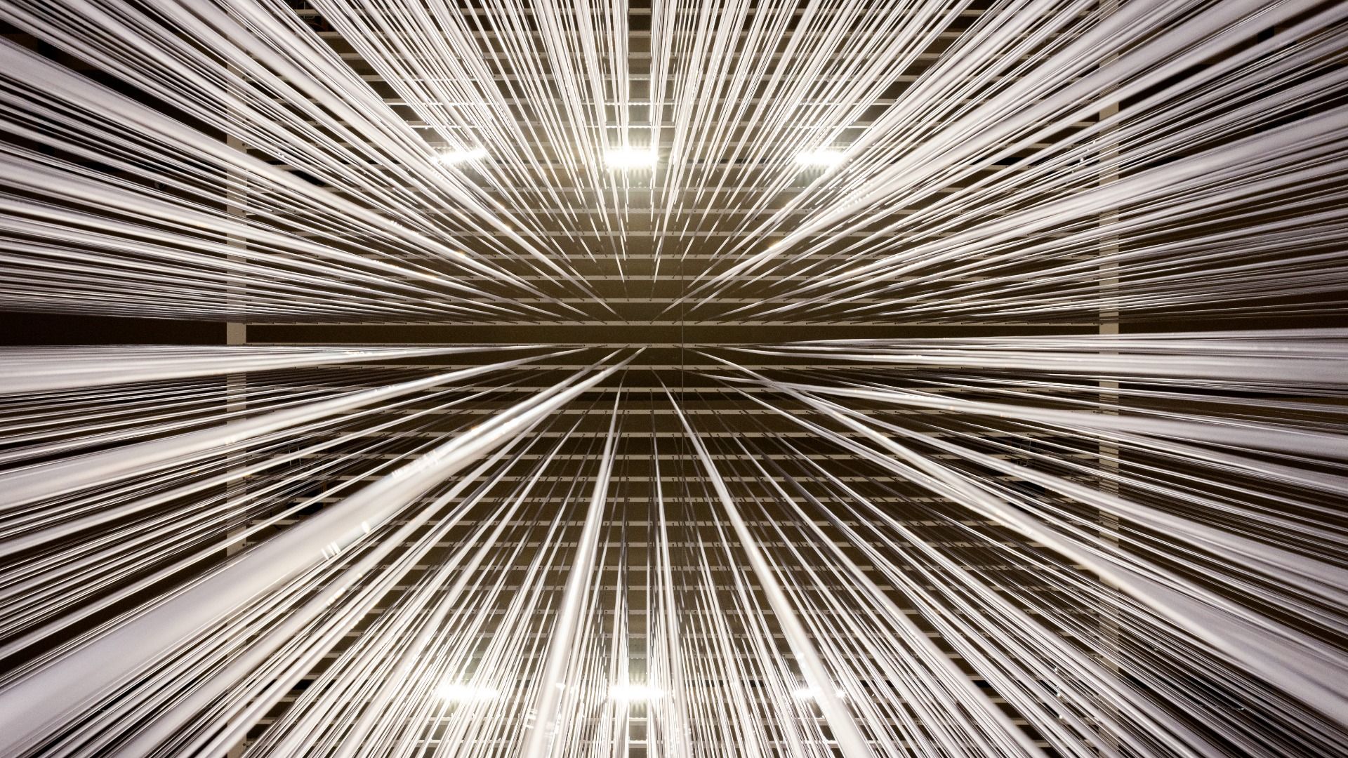 Abstract installation with numerous thin white vertical lines converging towards the center, creating a sense of depth and radial symmetry against a dark background.