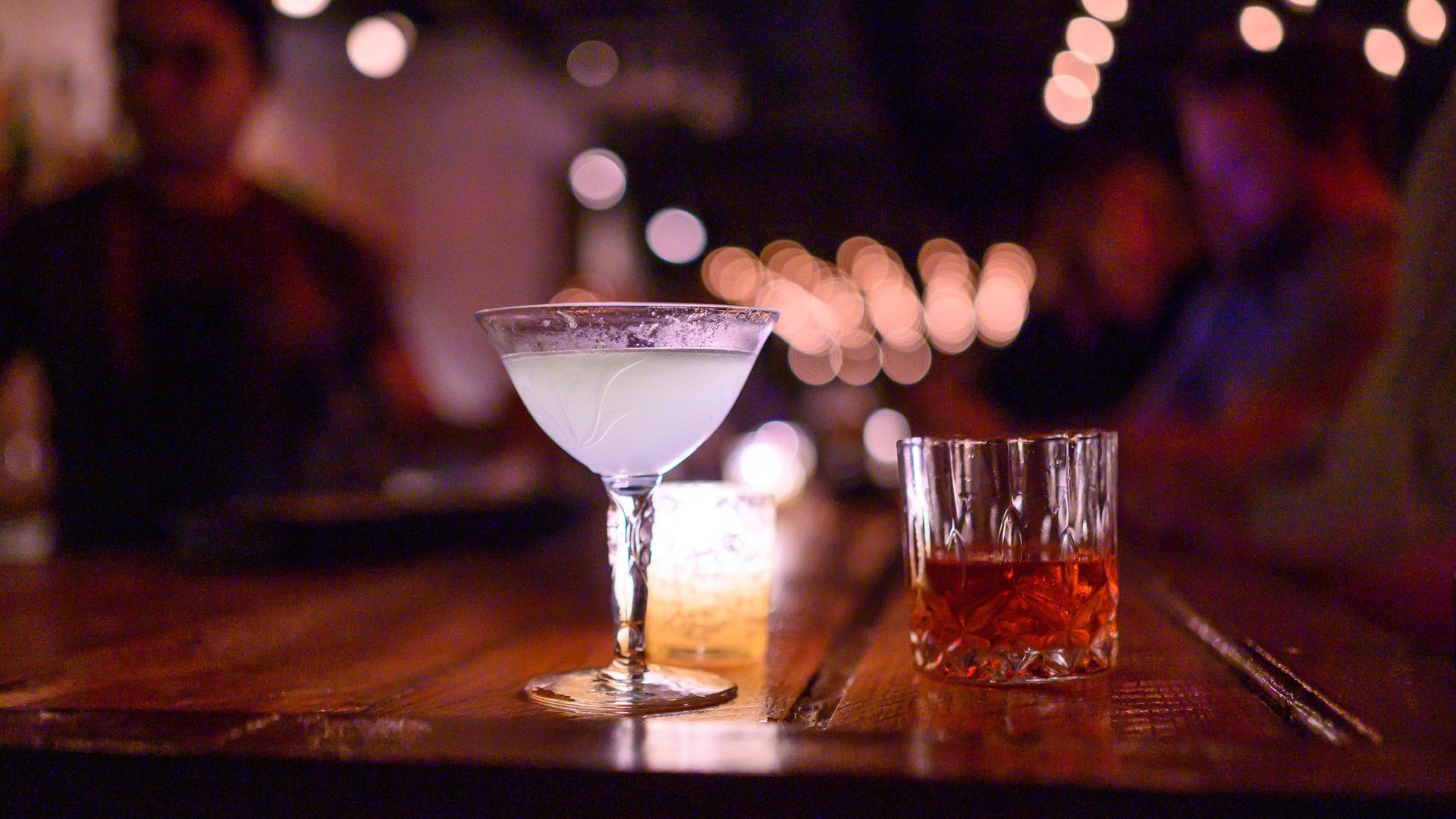 Two drinks on a wooden bar in a martini glass and a rocks glass