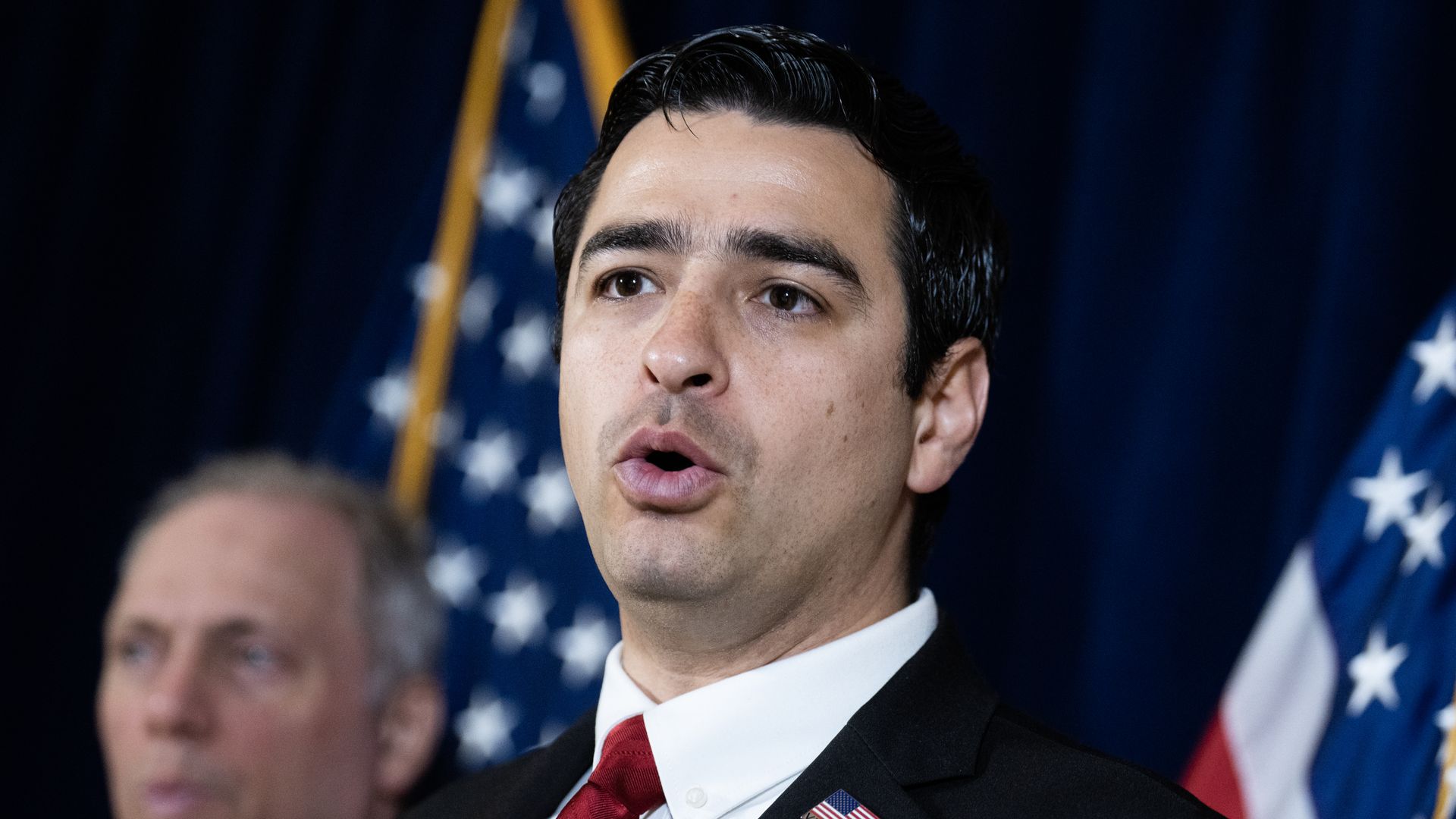 A man speaks while wearing a necktie and a white shirt.