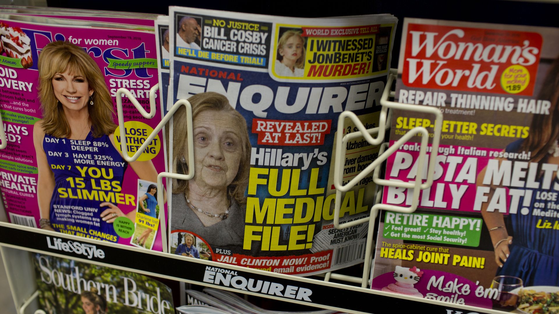 In this image, a stack of National Enquirer magazines sit between two others in a store rack. 