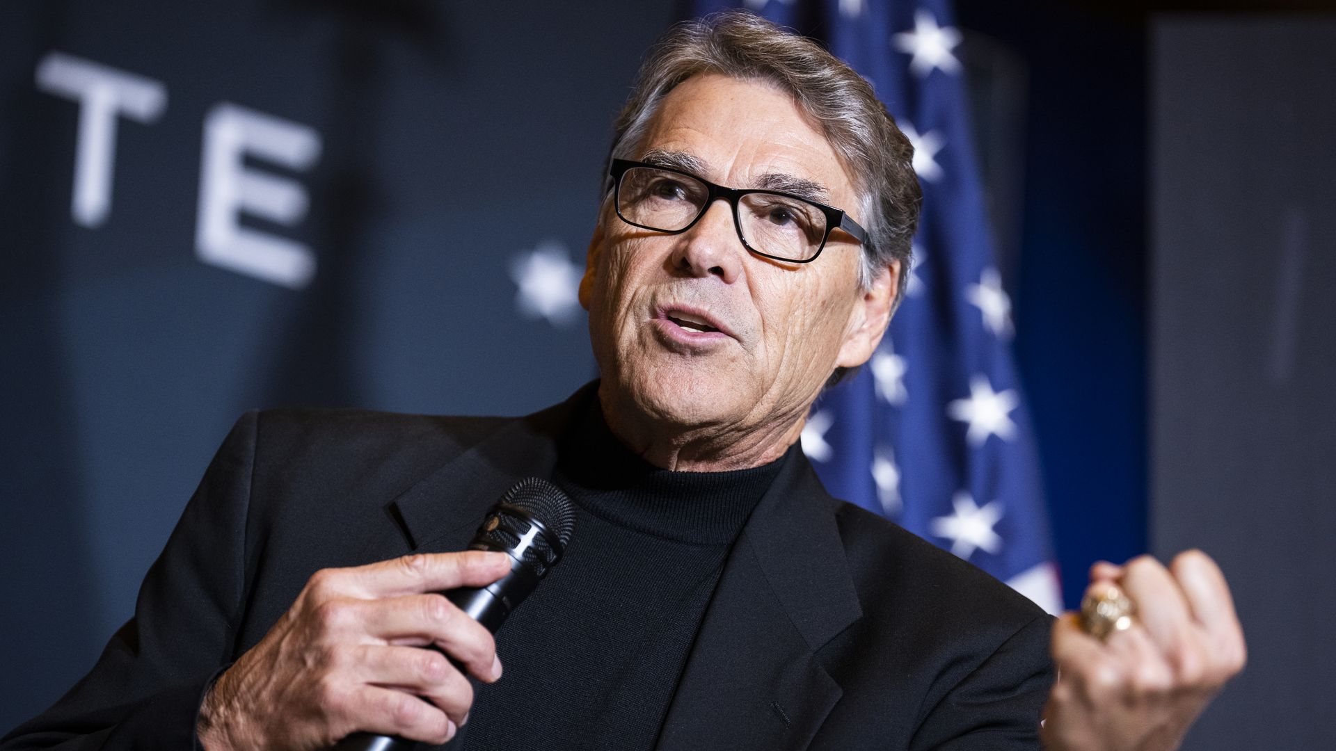 Rick Perry, in glasses, clenching a fist as he speaks into a microphone