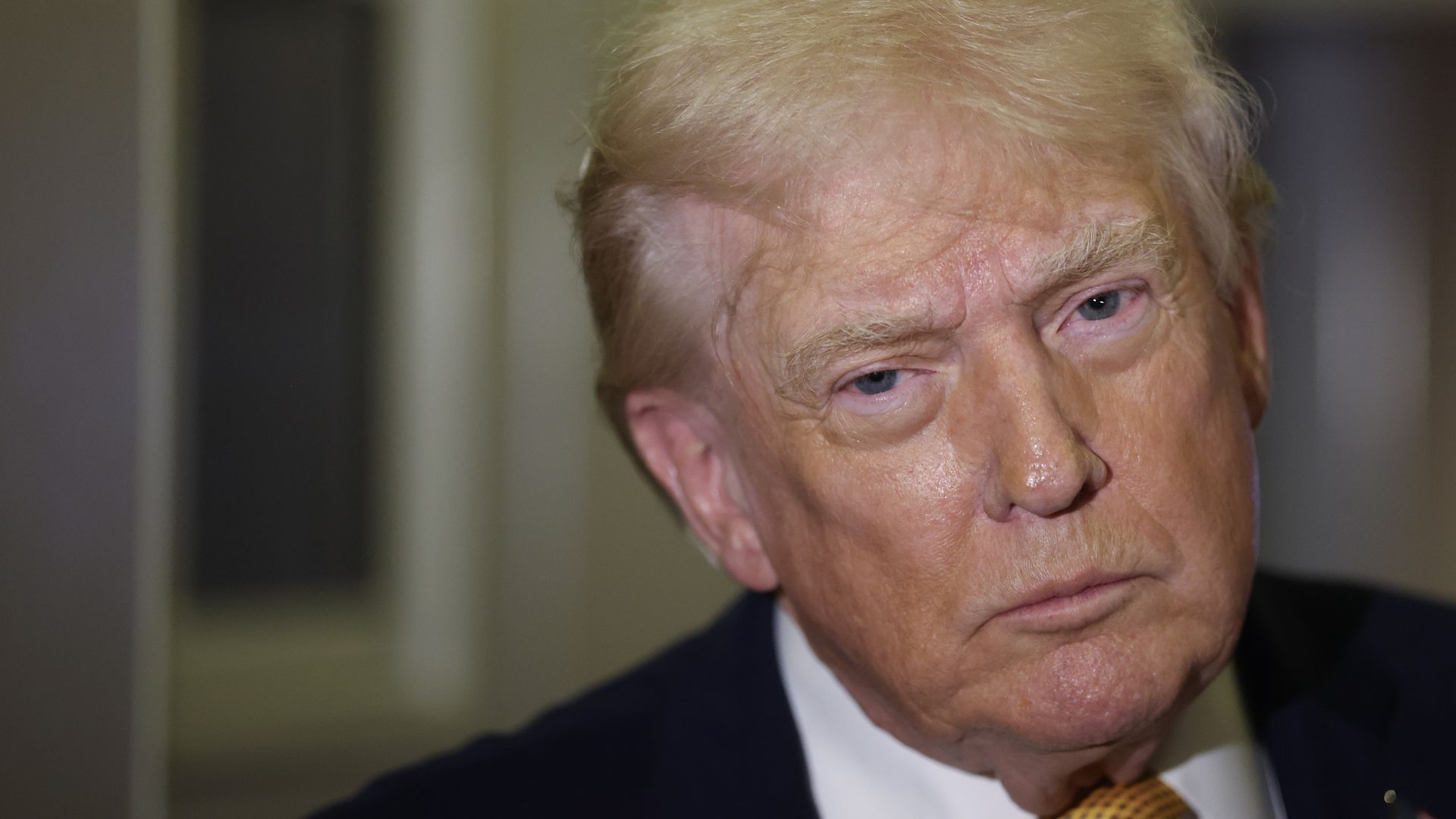 Trump wearing a blue suit jacket, white collared shirt and yellow patterned tie with an intent look 