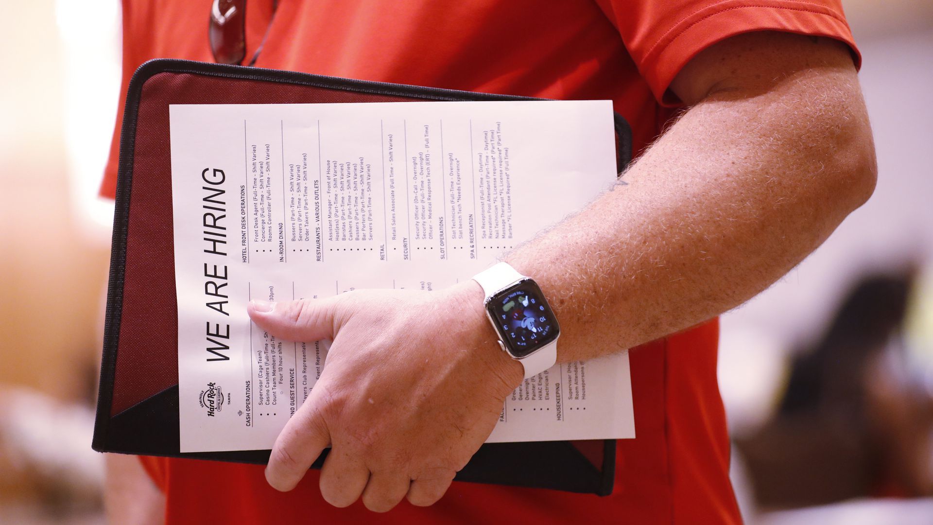 A hand clutches a portfolio with a paper on top that reads "We are hiring" in bold letters at a job fair at the Seminole Hard Rock Casino in May.