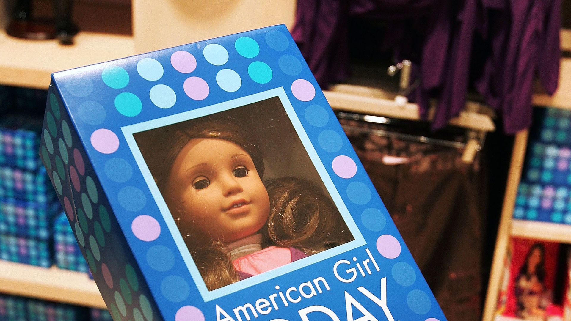 A picture of a hand holding an American Girl doll in a box