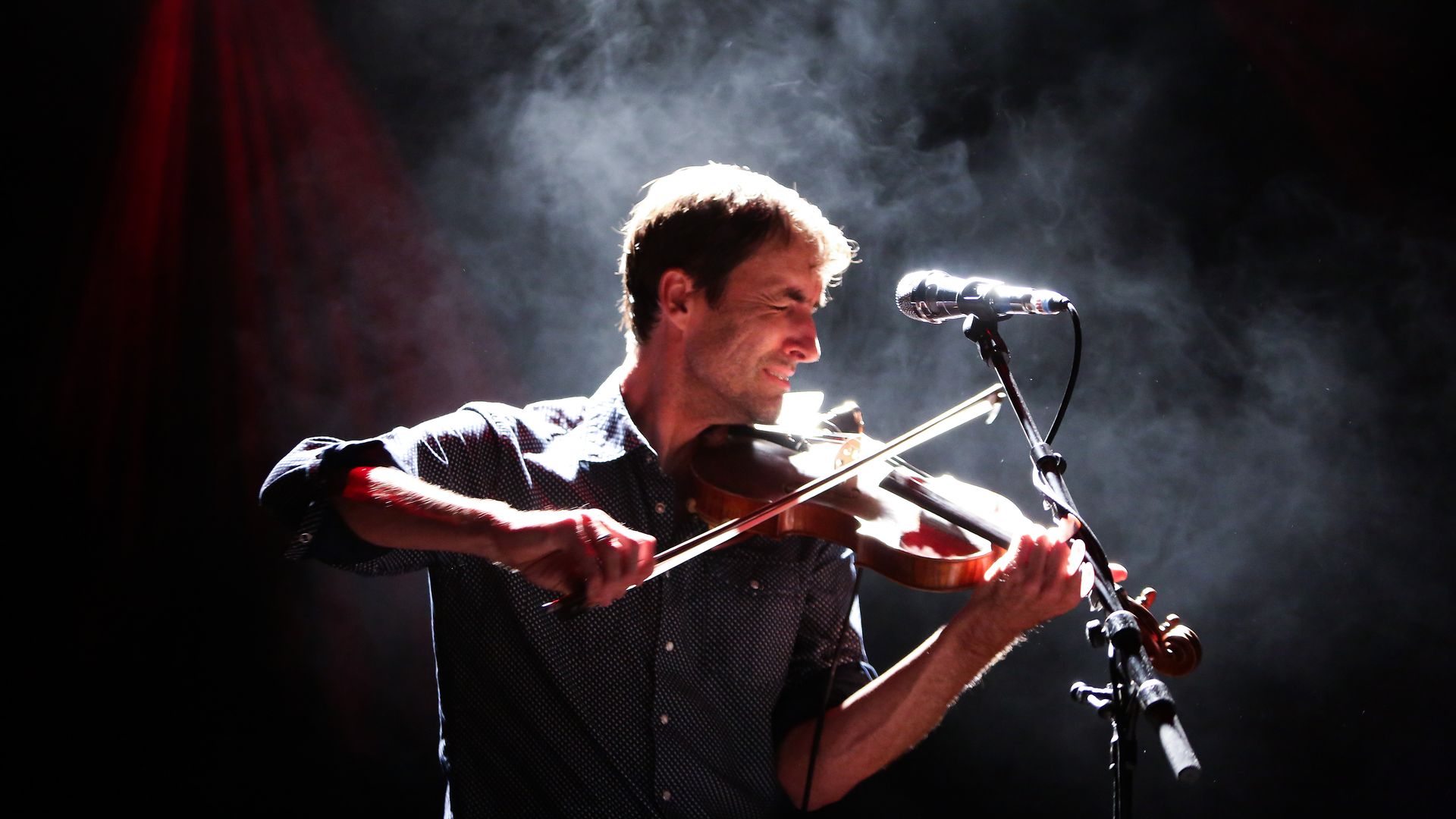 A backlit Andrew Bird playing a violin, surrounded by smoke