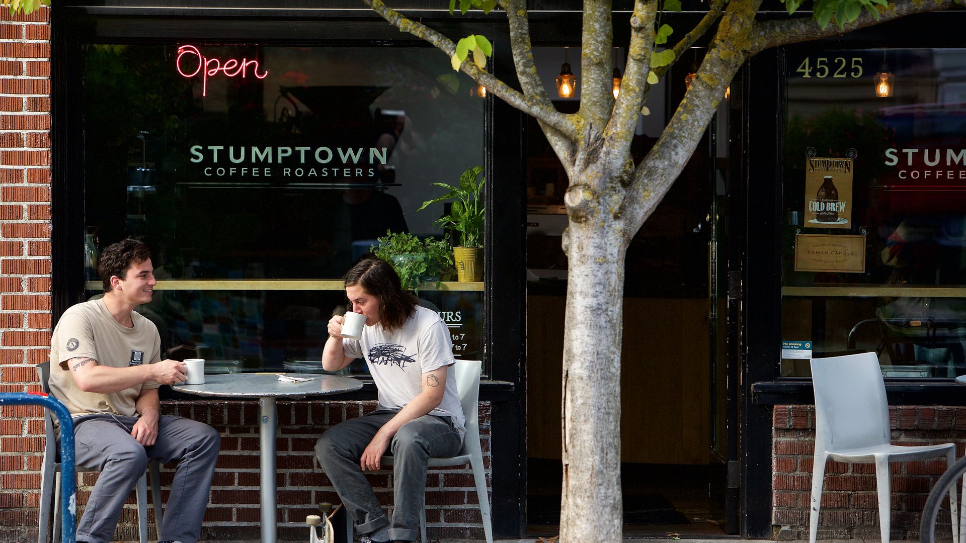 Two people drink coffee sitting outside.