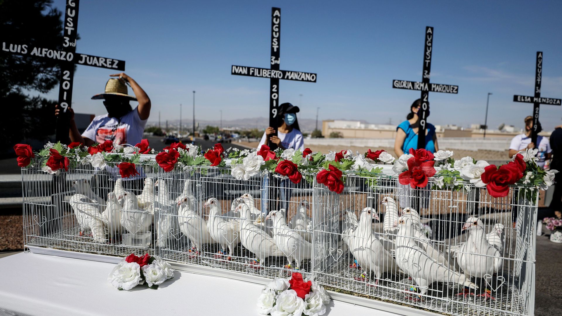 23 white doves wait in a cage to be released in El Paso. four women behind them are holding large crosses with the names of victims of a mass shooting in 2019.