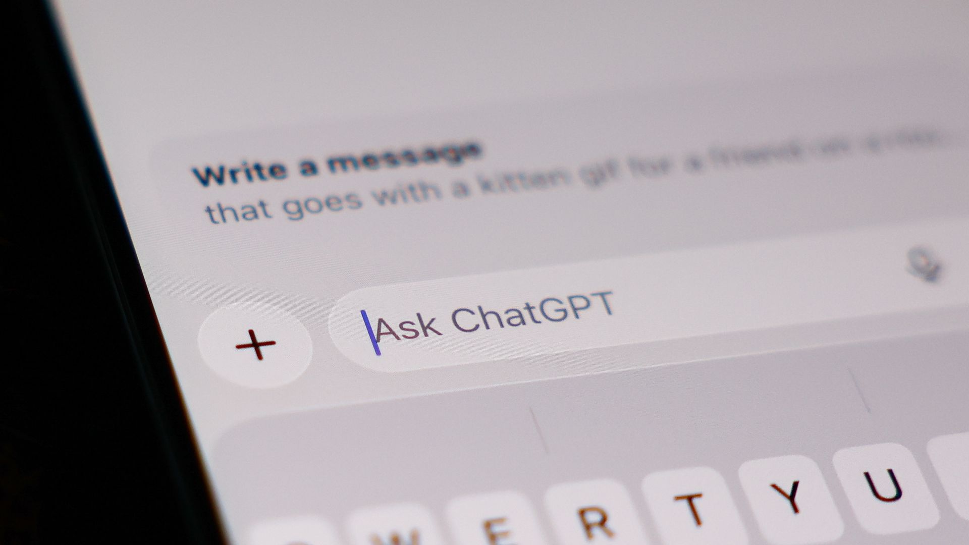 Close-up of a smartphone screen showing a chat interface: the text field reads "Write a message"; a purple "Ask ChatGPT" button is visible, with a red plus icon and a blurred QWERTY keyboard below.